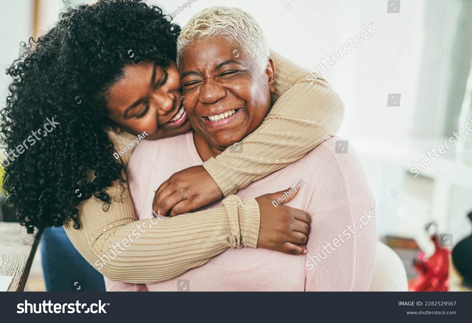 African daughter hugging her mum indoors at home - Main focus on senior mother face - Mom day and family love concept #2282529567