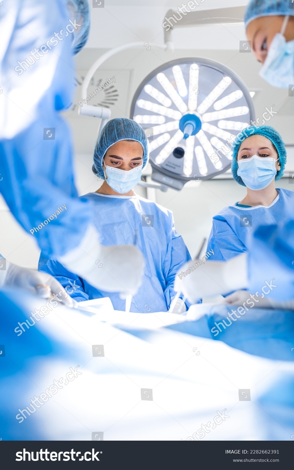 Group of surgeons wearing safety masks performing operation. Medicine concept. surgery, medicine and people concept - group of surgeons at operation in operating room at hospital #2282662391