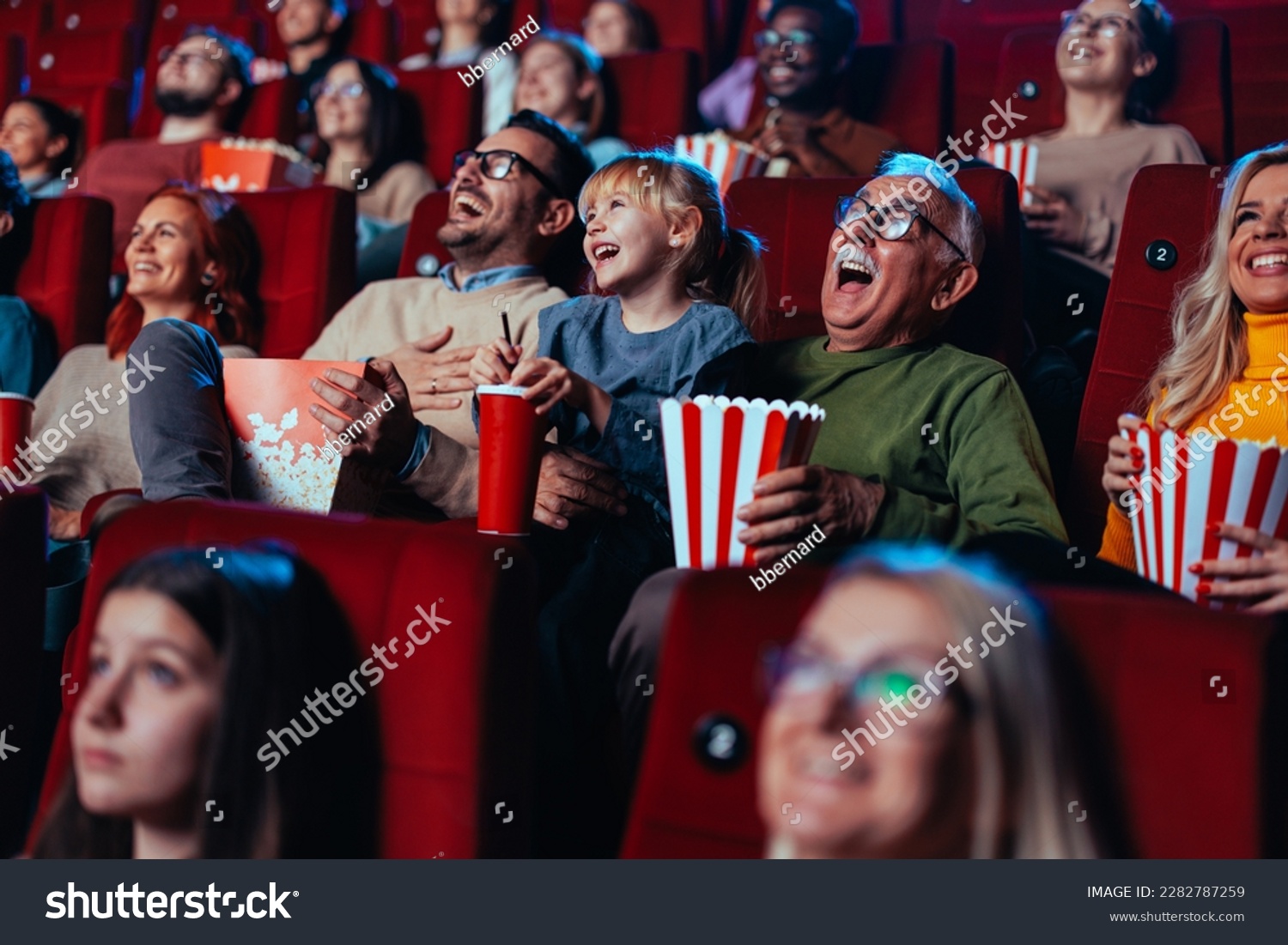 A grandfather and his granddaughter are in the movies enjoying themselves and having fun laughing out loud. #2282787259