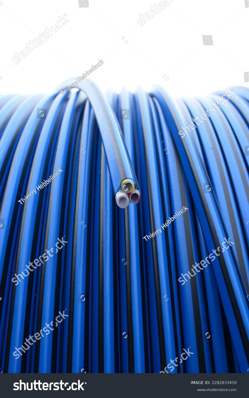 Close up on outdoor blue and black colored optical fiber tube coil with 3 tubes inside, blue, yellow and red striped #2282833459