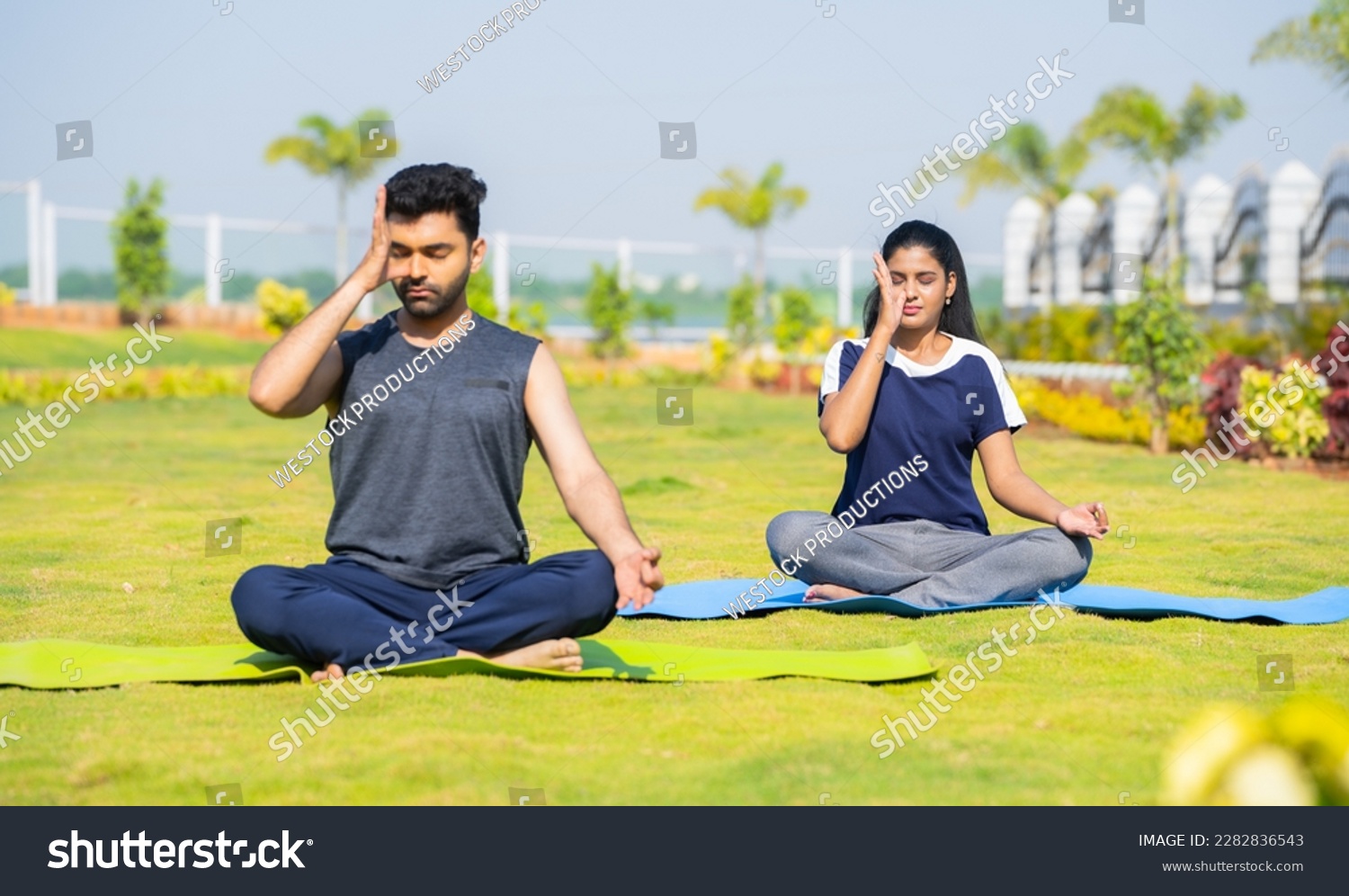 Young couple doing yoga or pranayama with eyes closed during morning at park - concept of healthy lifestyles, mindfulness and morning rituals #2282836543