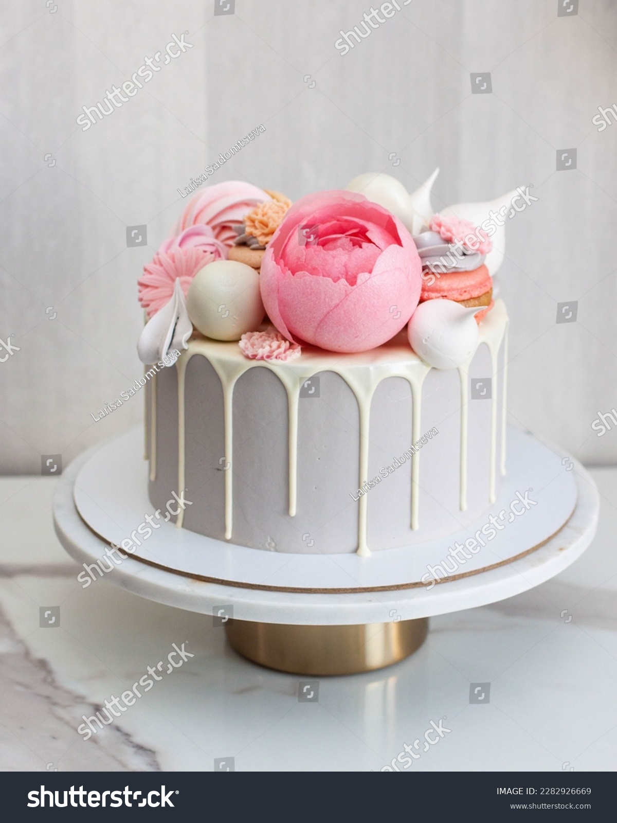 Beautiful and elegant grey cake decorated with melted white chocolate, macaroons, pink peony flower, cake pops and candies on marble cakestand #2282926669