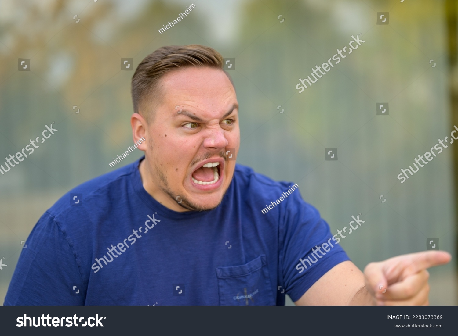Extremely angry aggressive young man yelling and pointing at someone #2283073369
