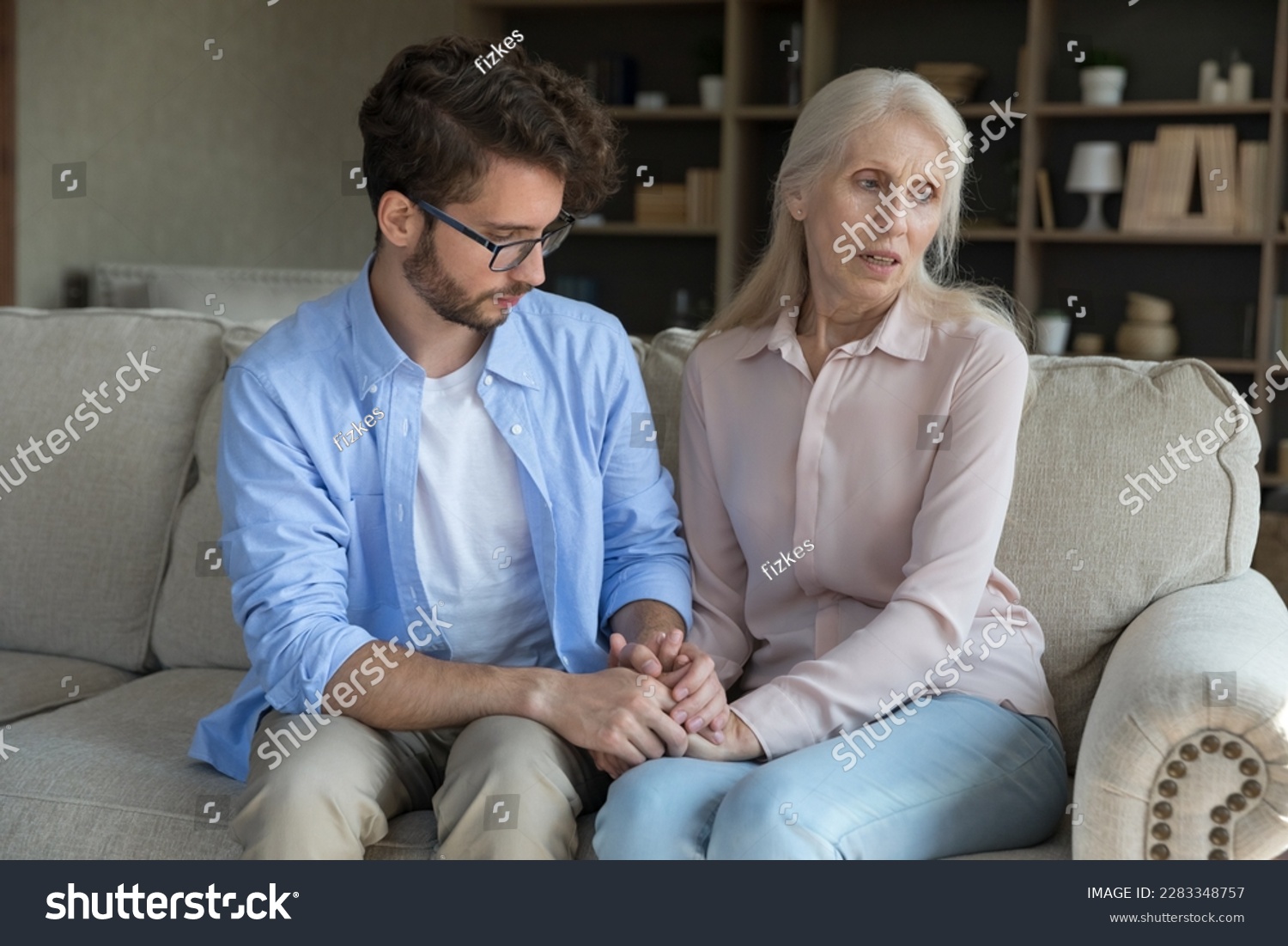 Loving adult son comforting worried concerned senior mother, sitting on couch, holding hand of elder mom, giving support, compassion, empathy, going through crisis, stress, bad news #2283348757
