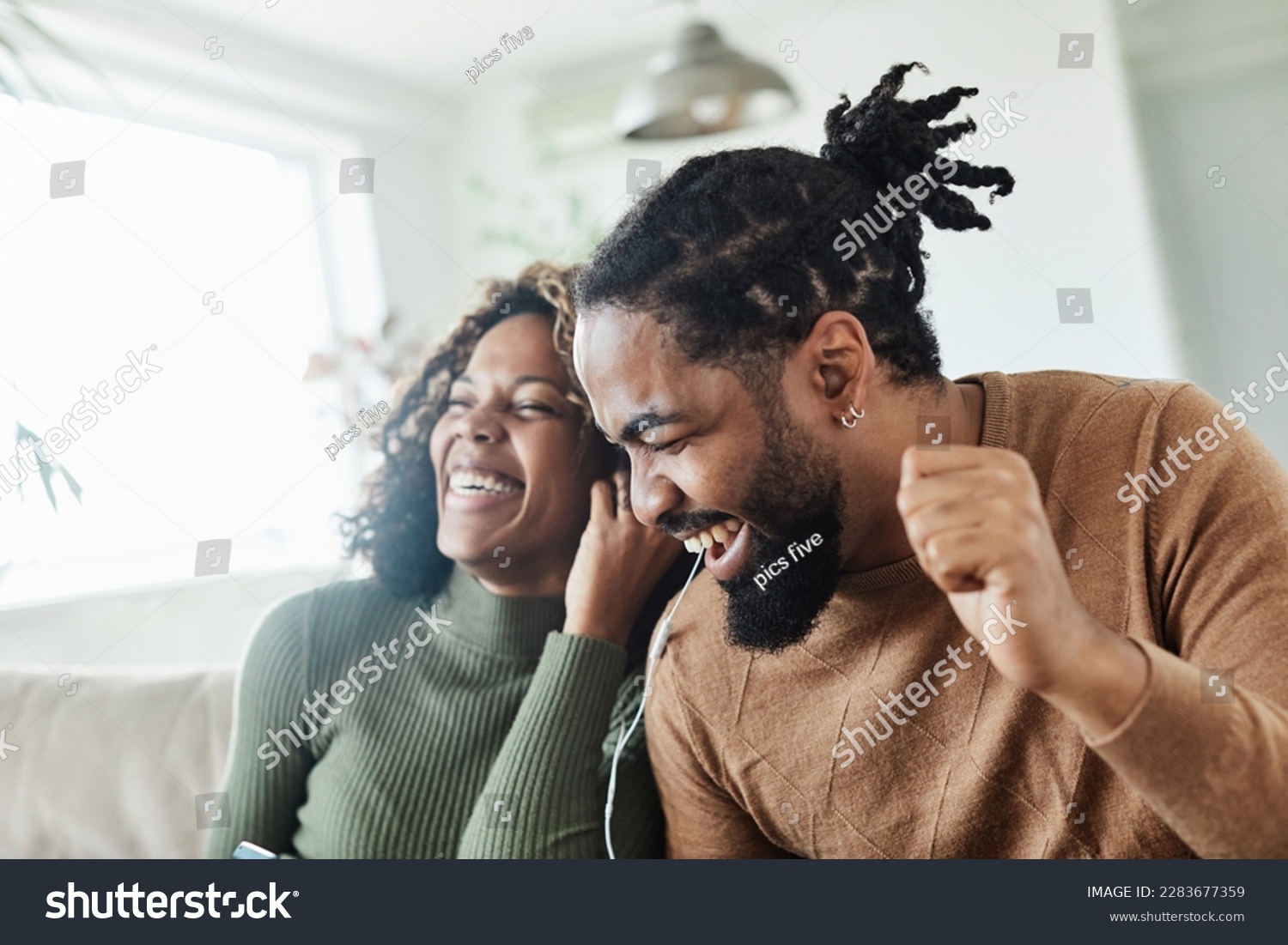 Portrait of a lovely young couple having fun and listening music wearing earphones and holding tablet together at home #2283677359
