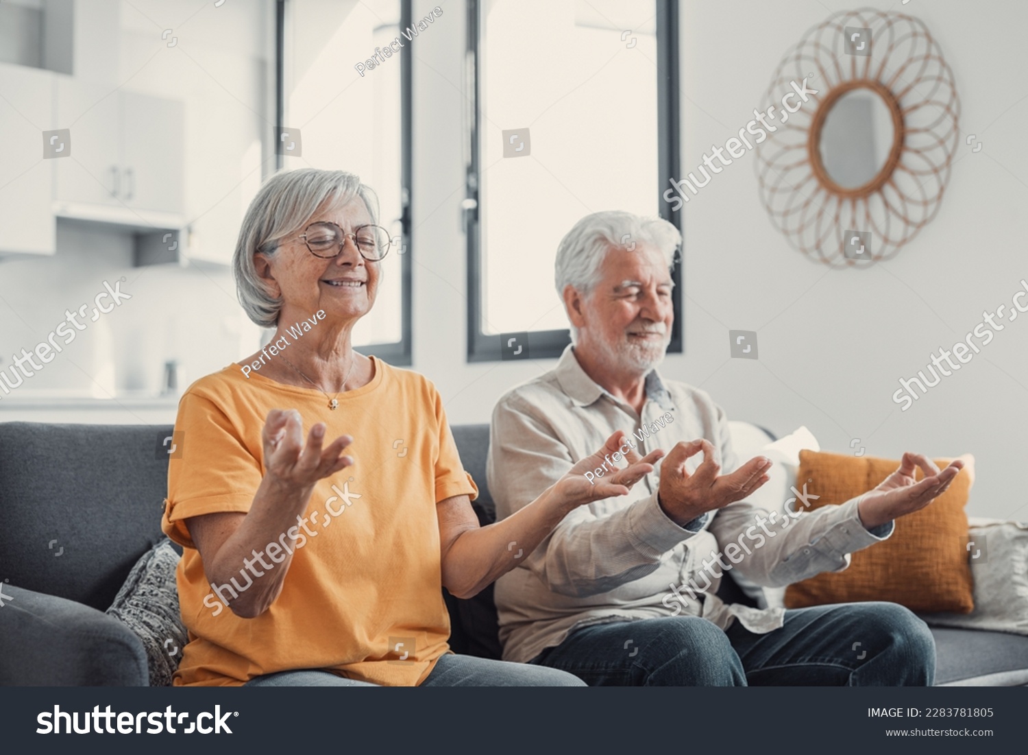 Calm senior middle aged couple practicing yoga together sitting in lotus pose on sofa, mindful peaceful mature man and woman meditating relaxing in living room at home, old people healthy lifestyle #2283781805