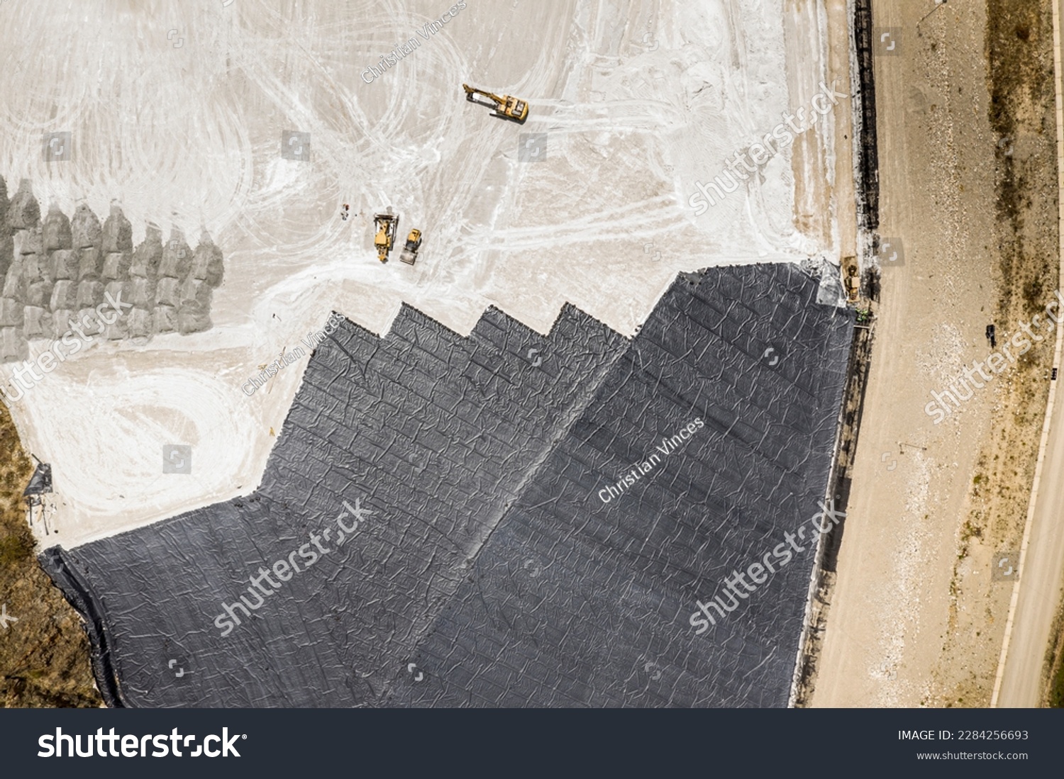 Aerial view of remediation work on a terrain with mining waste fillings, where working machinery and high-density geomembrane cover can be seen. #2284256693