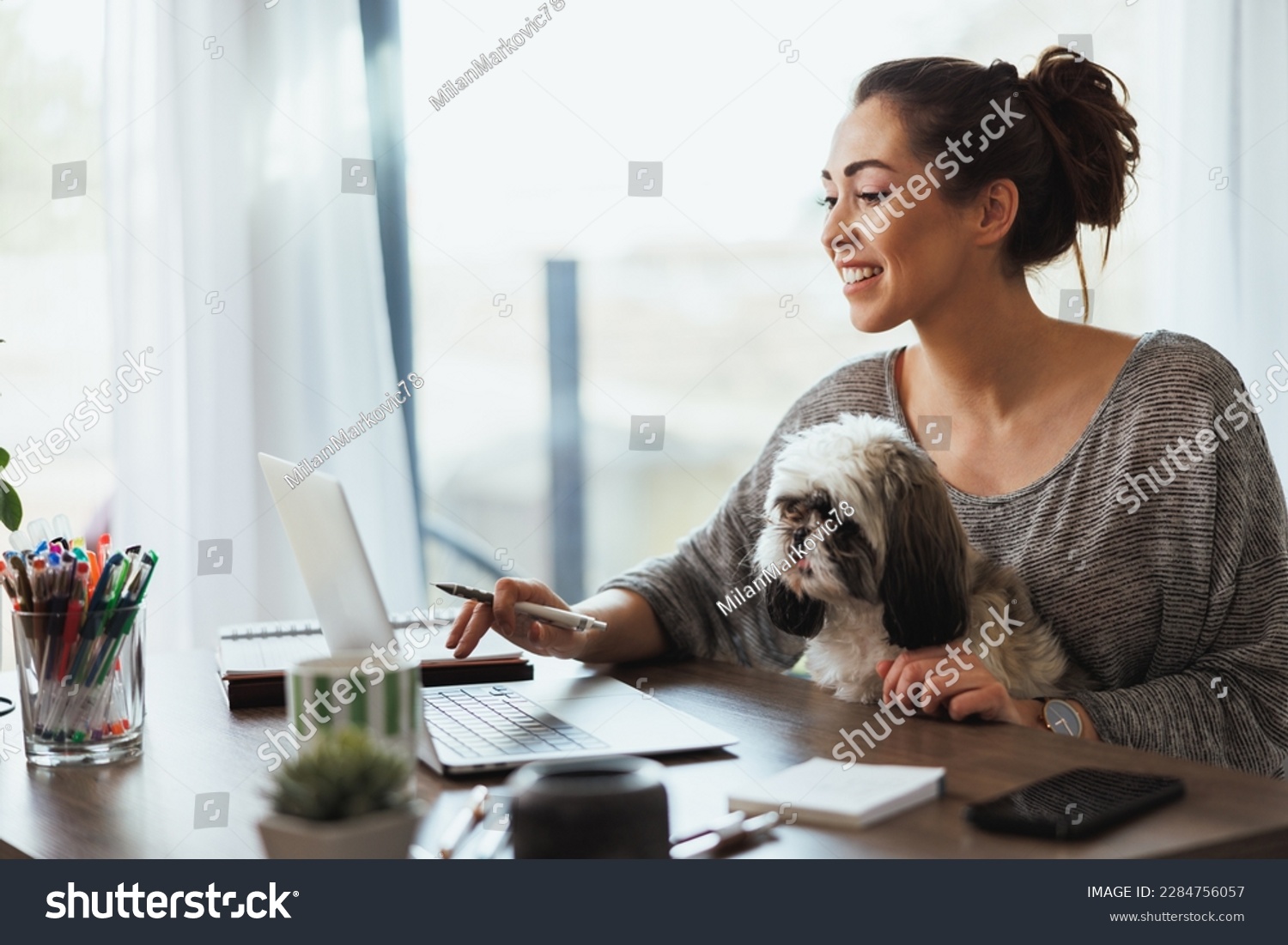Attractive young female freelancer working on laptop from her home and having her pet dog in her lap to keep her company. #2284756057