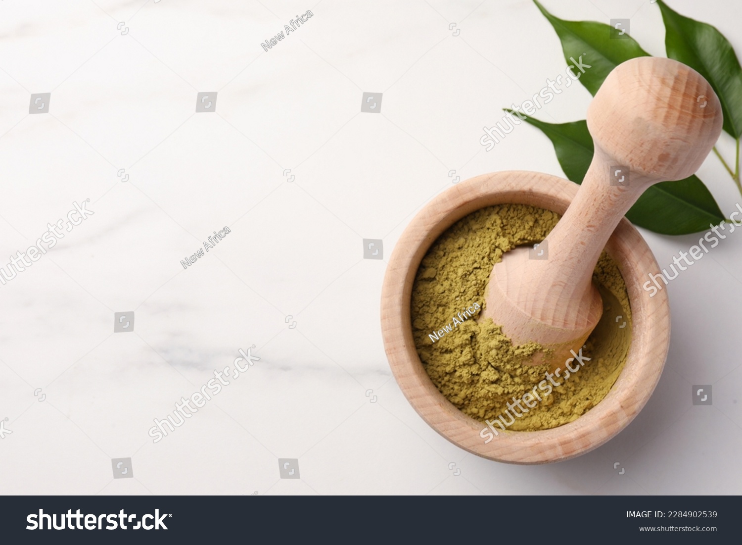 Mortar of henna powder and green leaves on white marble table, top view with space for text. Natural hair coloring #2284902539