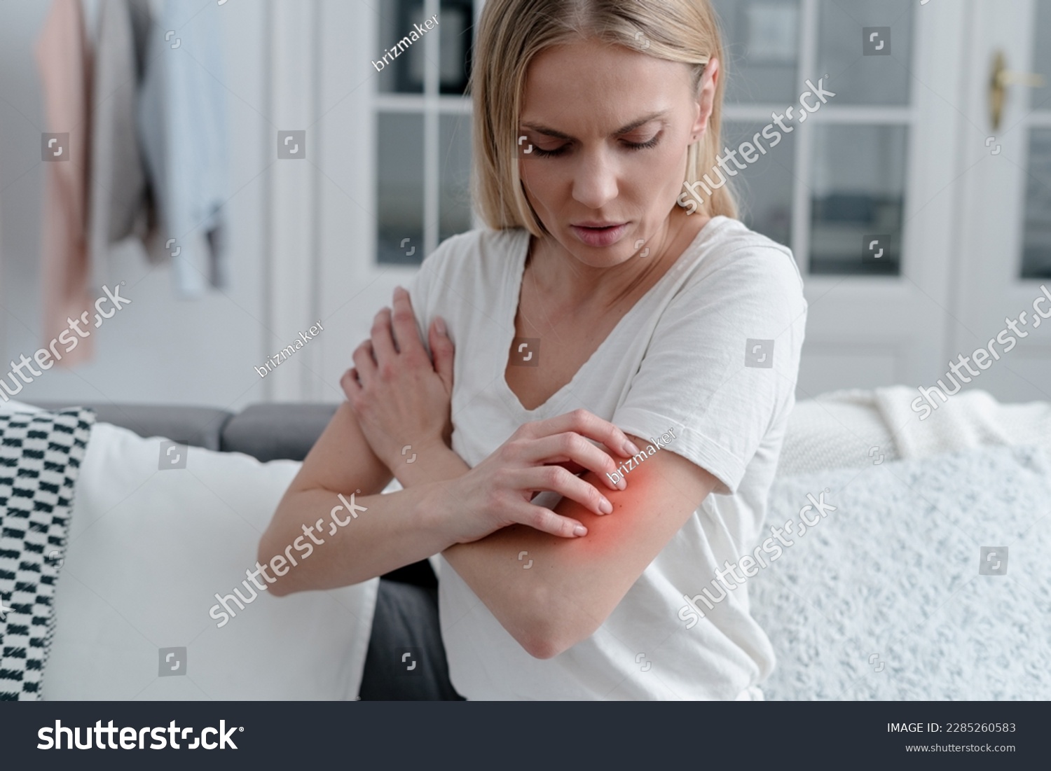 worried female feeling unwell, has allergy or reaction from insect bite, girl with itch or irritation on arm sitting on sofa in room  #2285260583
