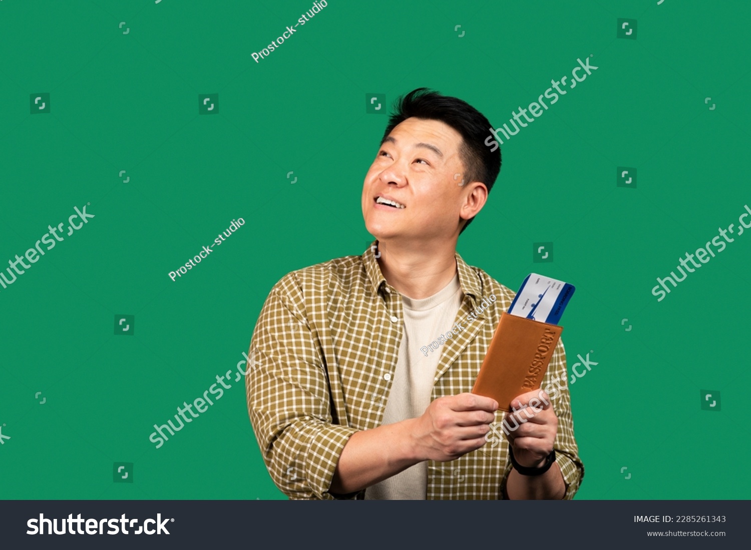 Portrait of asian middle aged man holding passport with plane boarding pass tickets, looking aside at copy space on green studio background. Overseas tourism, abroad vacation concept #2285261343