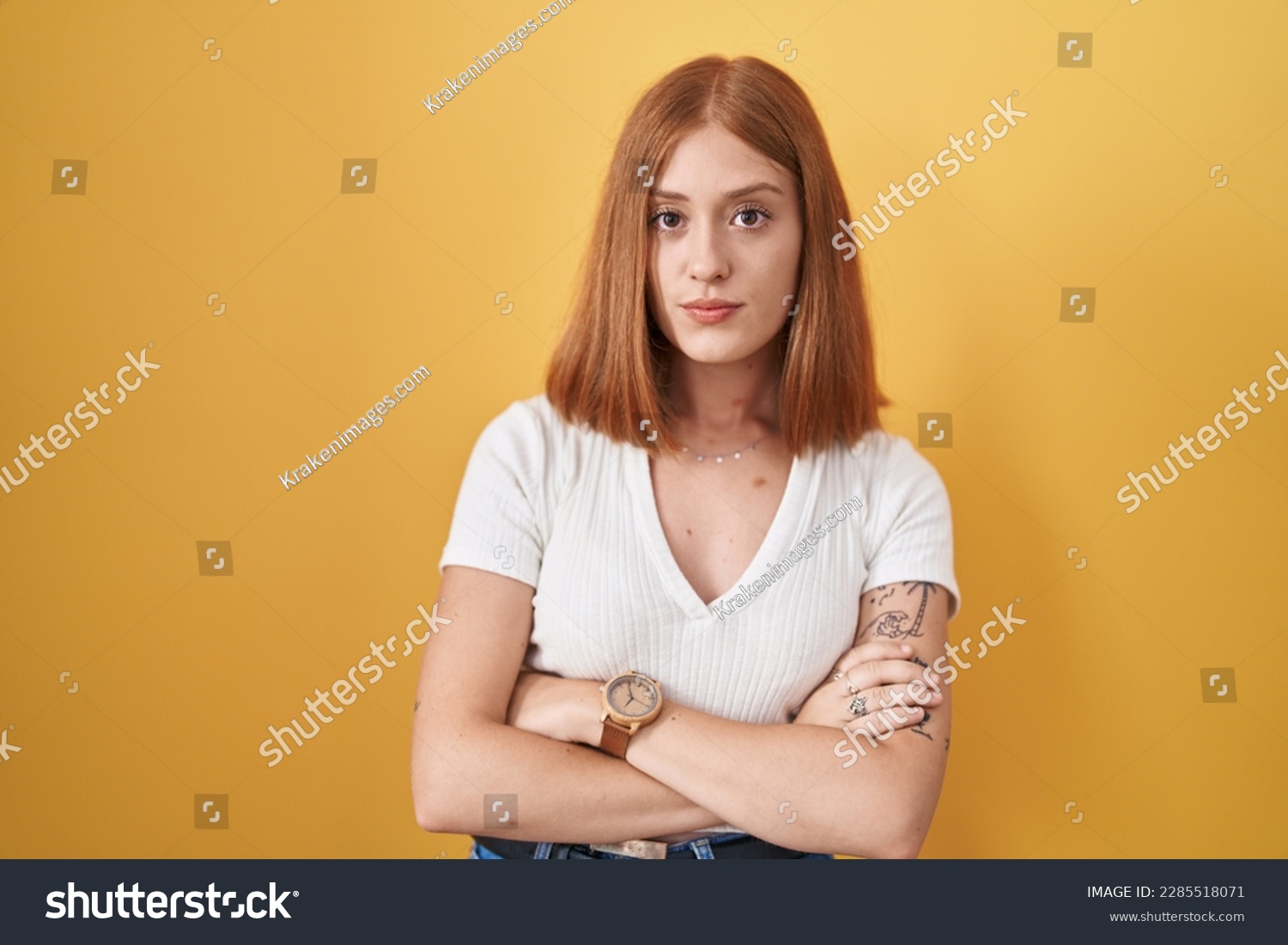 Young redhead woman standing over yellow background skeptic and nervous, disapproving expression on face with crossed arms. negative person.  #2285518071