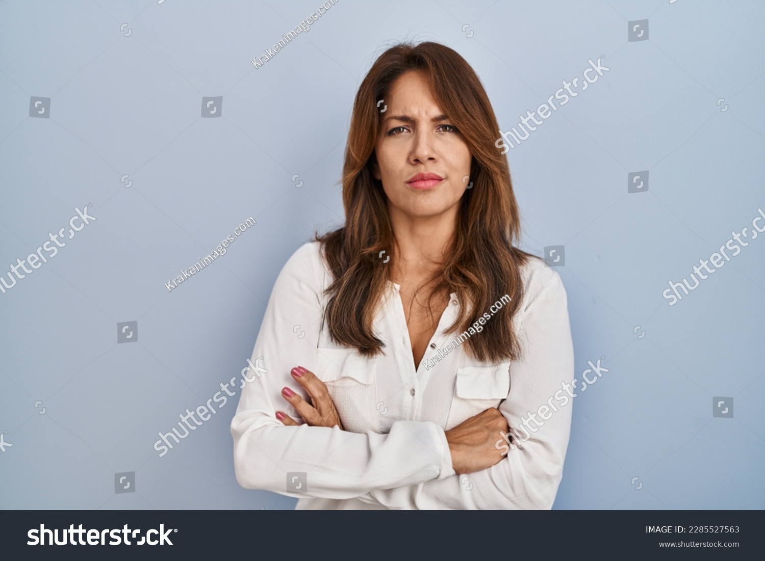 Hispanic woman standing over isolated background skeptic and nervous, disapproving expression on face with crossed arms. negative person.  #2285527563