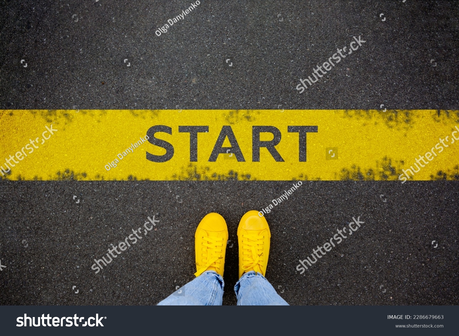 Female feet in yellow sneakers standing on street background with word new start written. Yellow race line beginning idea concept. Top view. Businessman of starting #2286679663