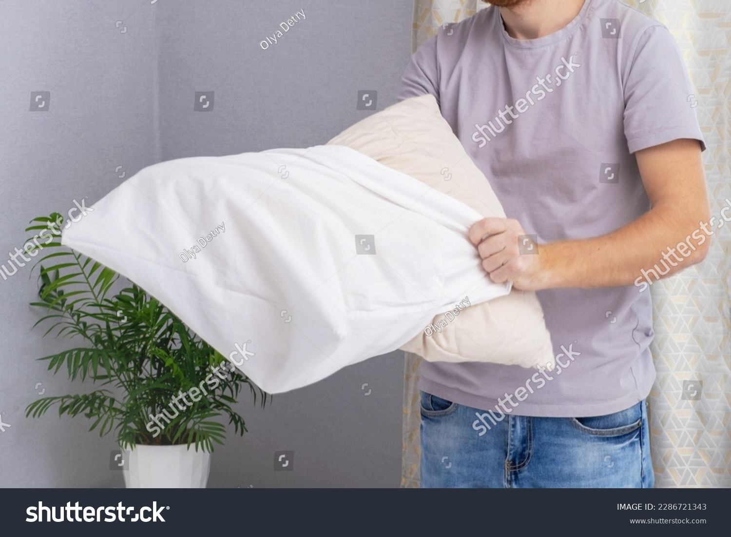A man tucks a pillow with a fresh bright white pillowcase. Making the bed with fresh bed linen by a white man. The day of the change of bed linen. The day of washing bed linen in the laundry room. #2286721343