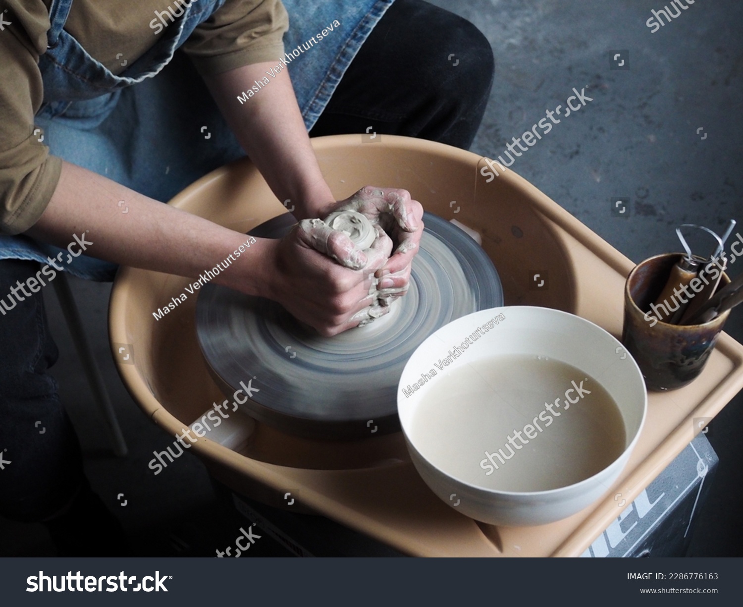 Young female master working on a potter’s wheel, creates clay dishes. Ceramist young woman making clay product on pottery wheel in her cozy studio. Small business, art, hobby, handcraft concept.	
 #2286776163