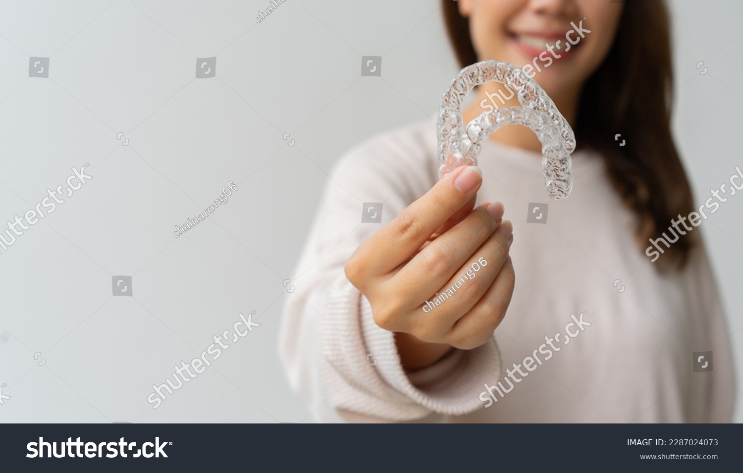 close up woman hand holding dental aligner retainer (invisible) on background for beautiful teeth and dental treatment course concept #2287024073