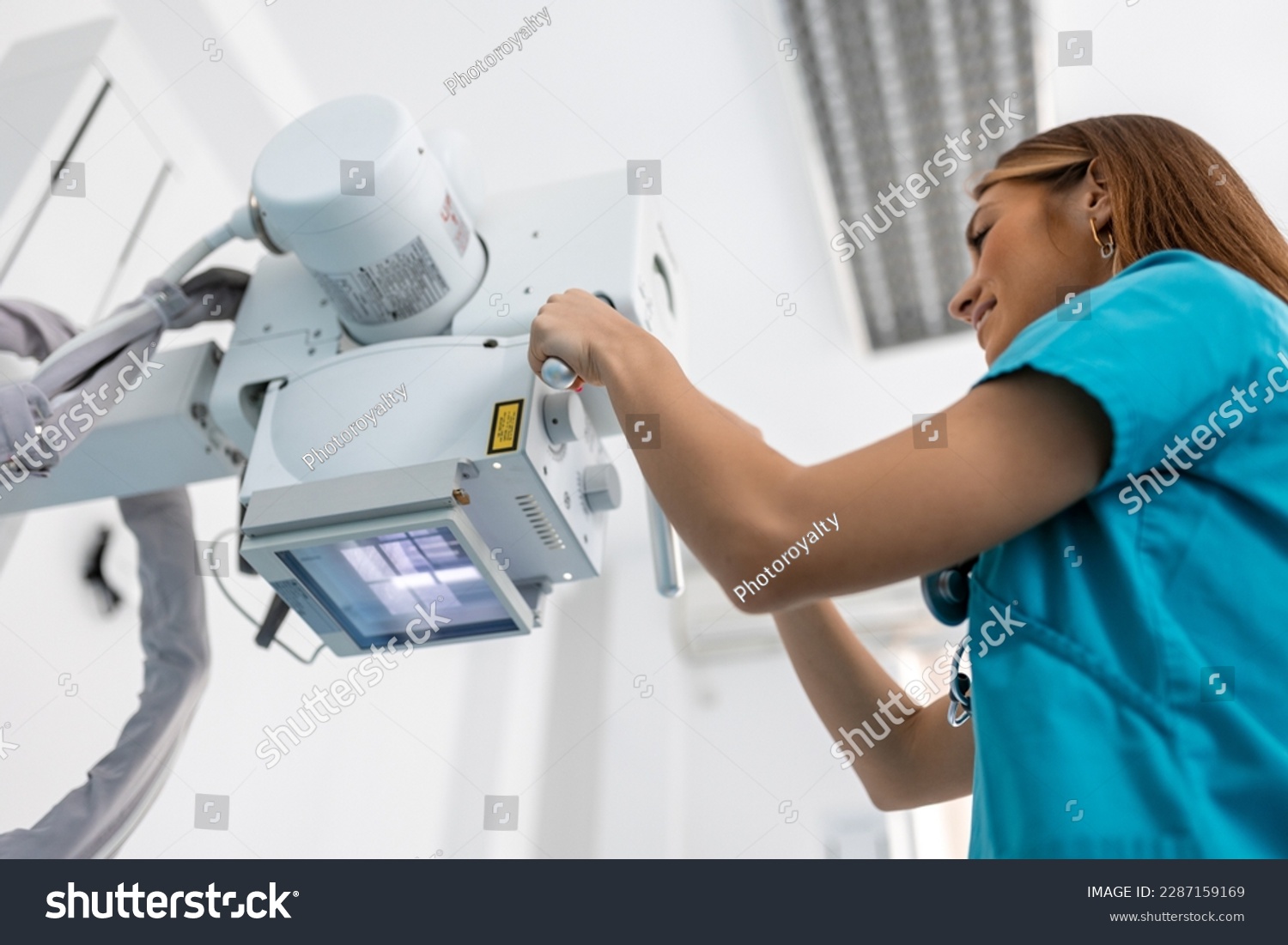 Doctor looking at X-ray machine in clinic. Female doctor sets up the machine to x-ray over patient. Radiologist and patient in a x-ray room. #2287159169