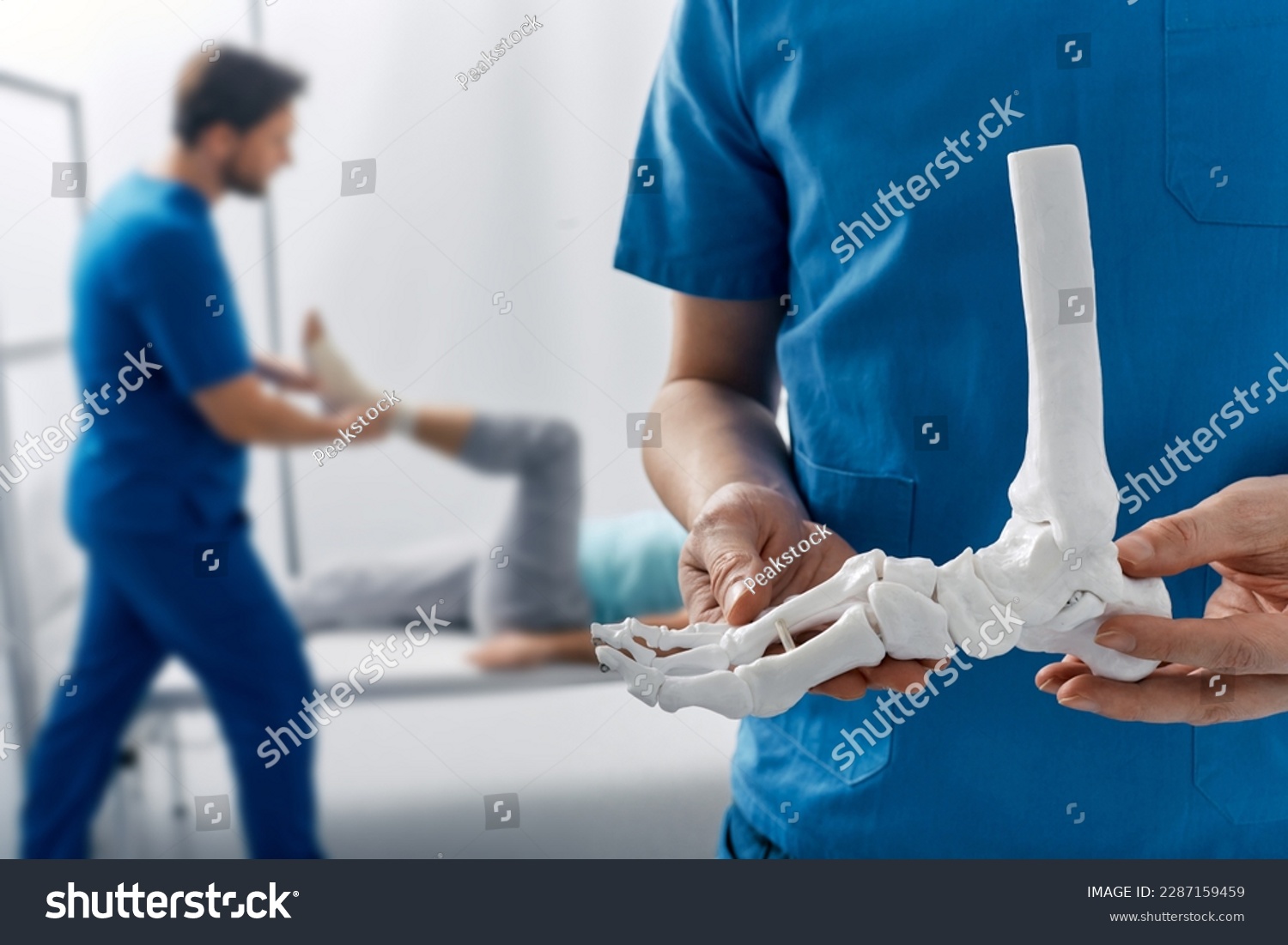 Podiatrist showing anatomical foot skeleton model during his assistant examination injured leg of patient in department of traumatology and orthopedics #2287159459