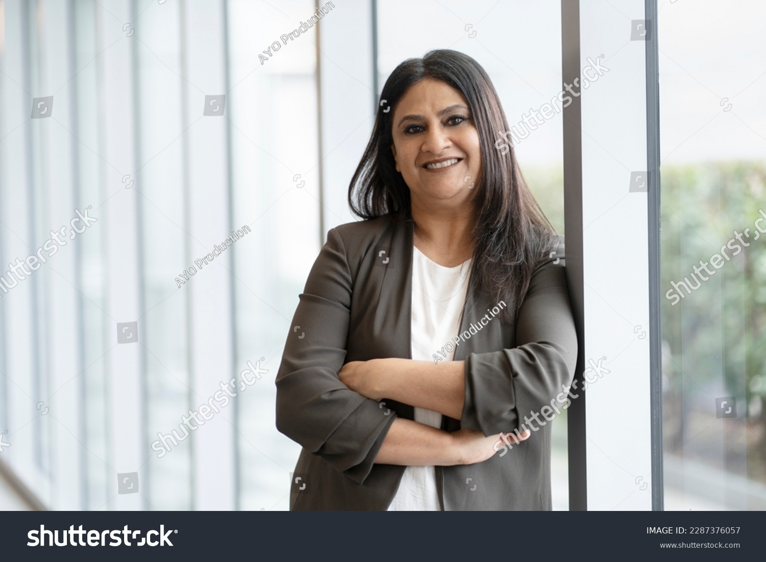 Confident smiling mature Indian businesswoman with arm crossed standing in modern office. Portrait of happy asian worker wearing stylish suit looking at camera indoors. Successful business concept  #2287376057
