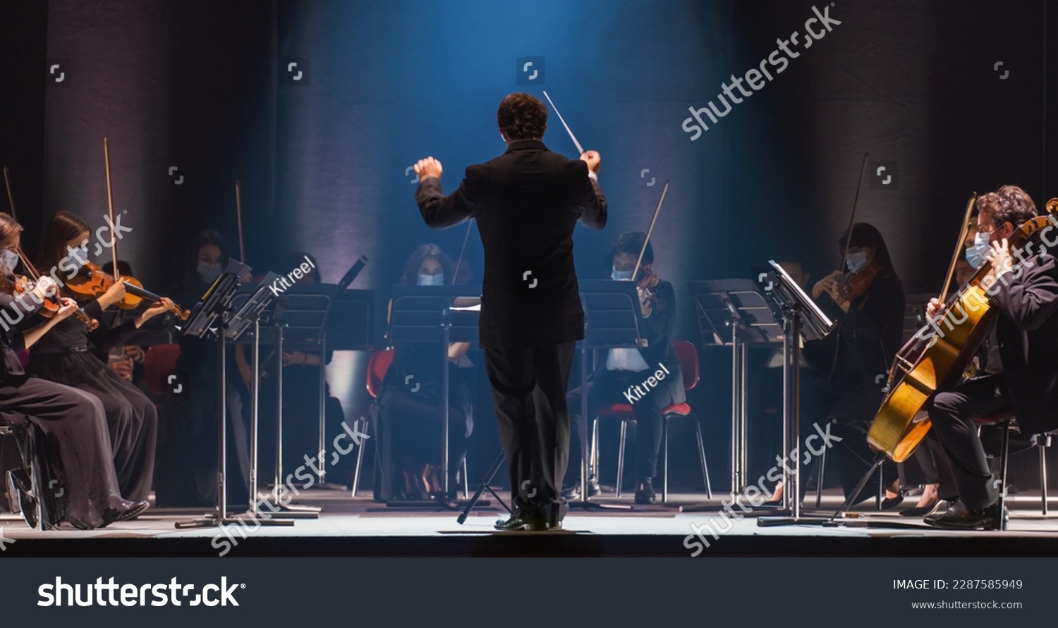 Cinematic Shot of an Orchestra on a Classic Theatre Stage: Professional Conductor Directing Symphony Orchestra with Performers Playing Violins, Cellos, and Trumpets During Music Concert #2287585949