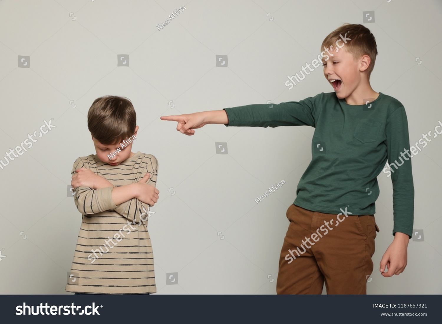 Boy laughing and pointing at upset kid on light grey background. Children's bullying #2287657321