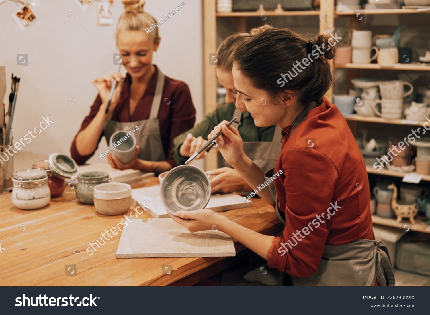 A company of three cheerful young women friends are painting ceramics in a pottery workshop. Have fun doing art. #2287908985