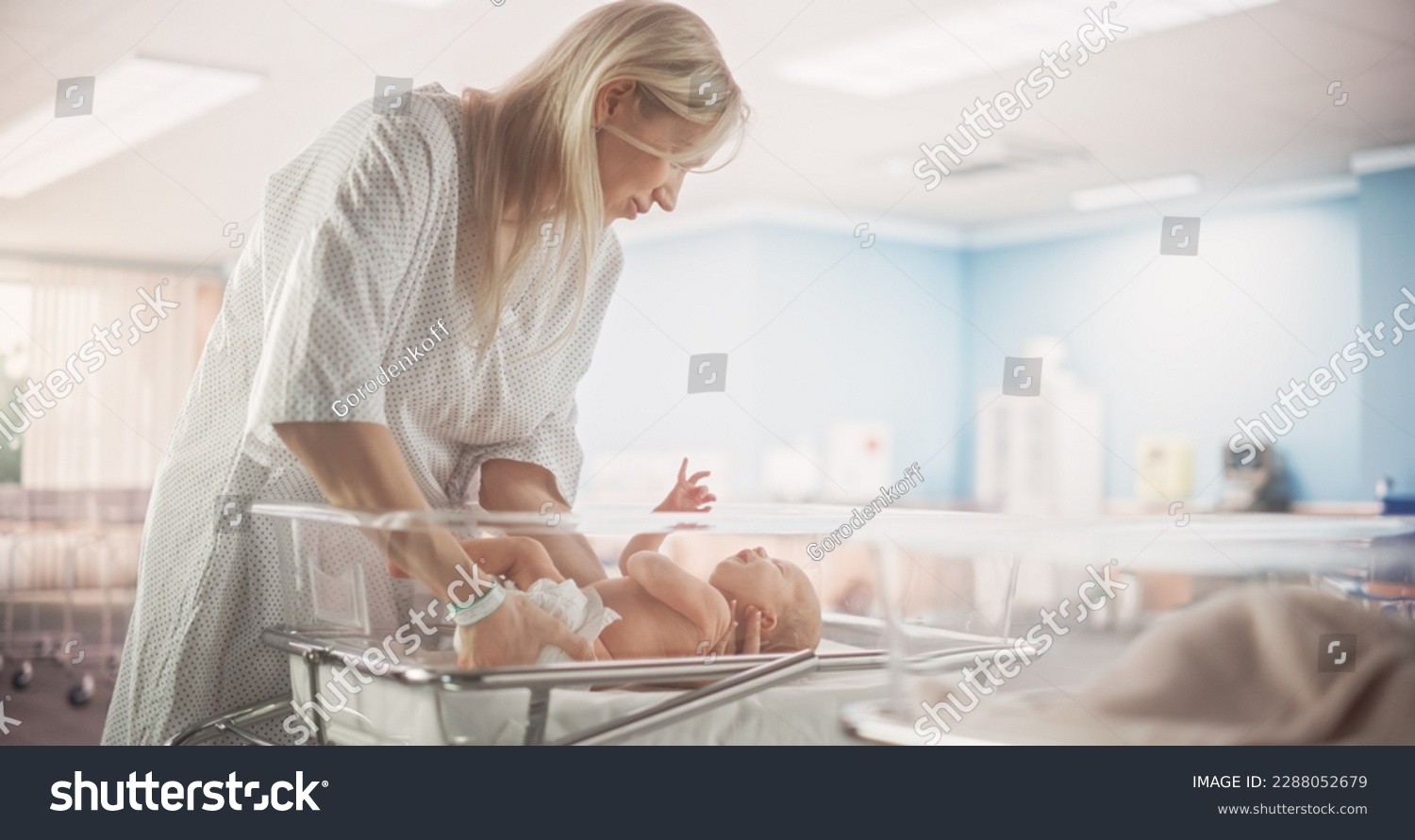 Mother Putting Down a Newborn Child on a Hospital Bassinet Bed in a Modern Nursery Clinic. Caring Mom Comforting Her New Born Child. Healthcare, Pregnancy and Motherhood Concept #2288052679