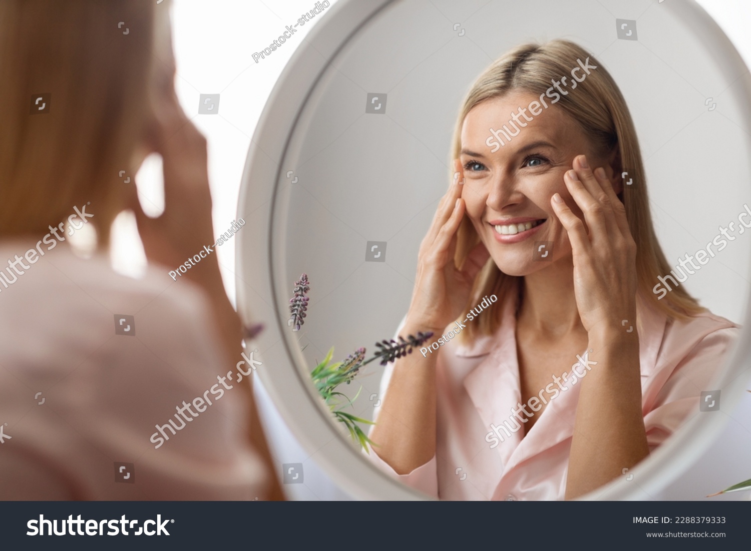 Beauty Concept. Portrait Of Attractive Mature Woman Looking At Mirror In Bathroom, Beautiful Middle Aged Lady Touching Her Flawless Face Skin And Smiling To Reflection, Selective Focus #2288379333