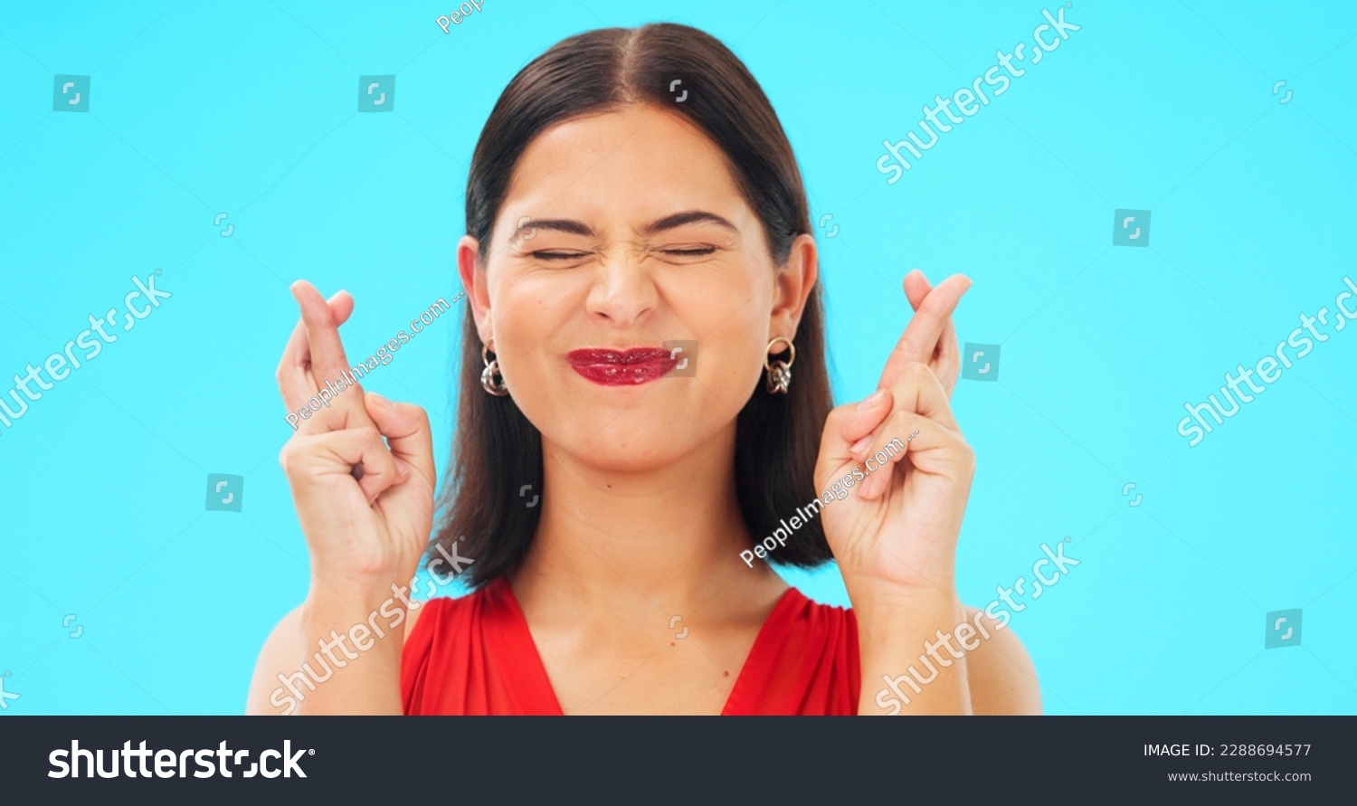 Happy, woman and face with fingers crossed on blue background, studio and wishing for good luck. Portrait of excited female model hope for winning prize, optimism and smile for emoji, hands and sign #2288694577