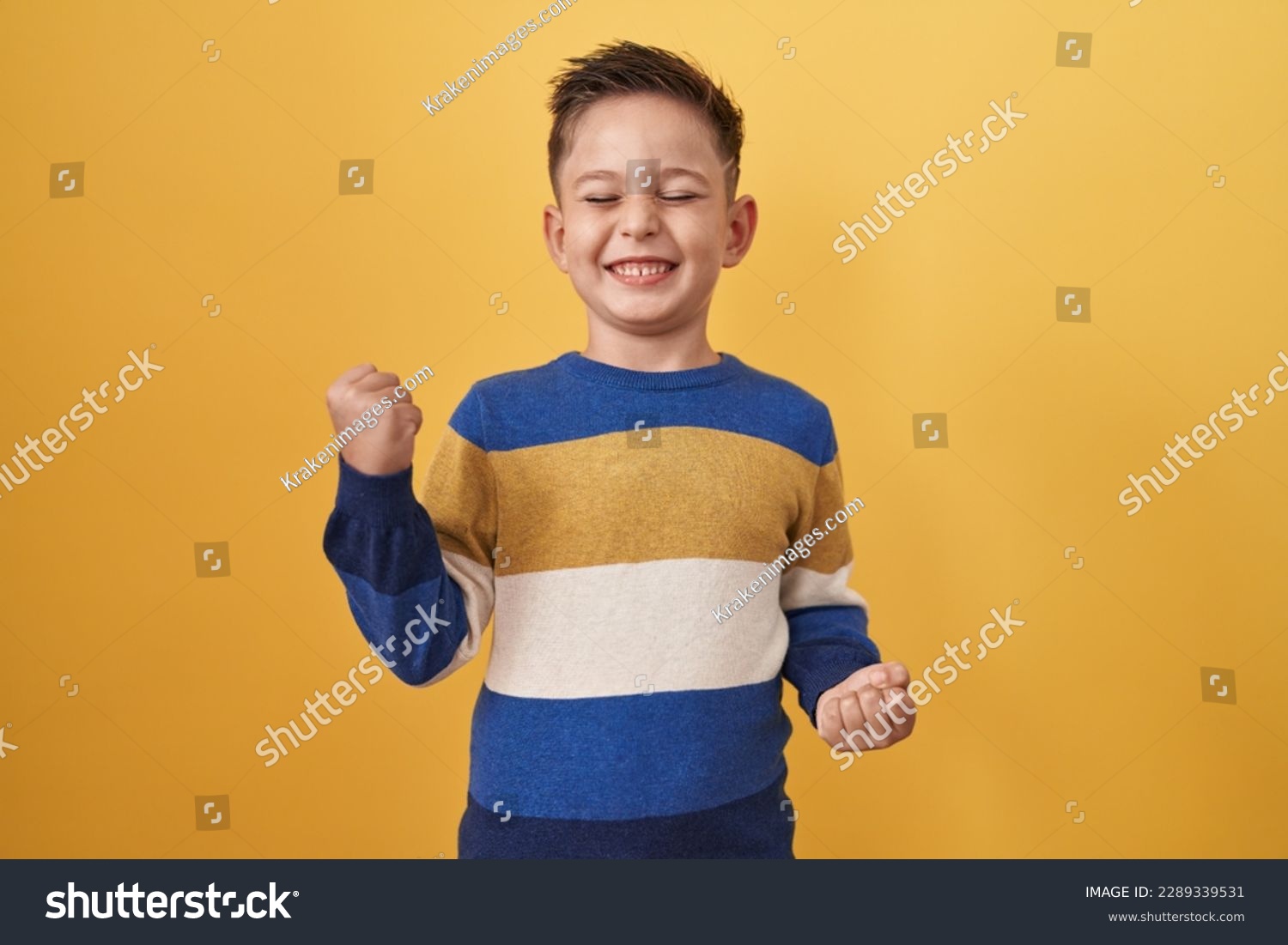 Little hispanic boy standing over yellow background celebrating surprised and amazed for success with arms raised and eyes closed  #2289339531