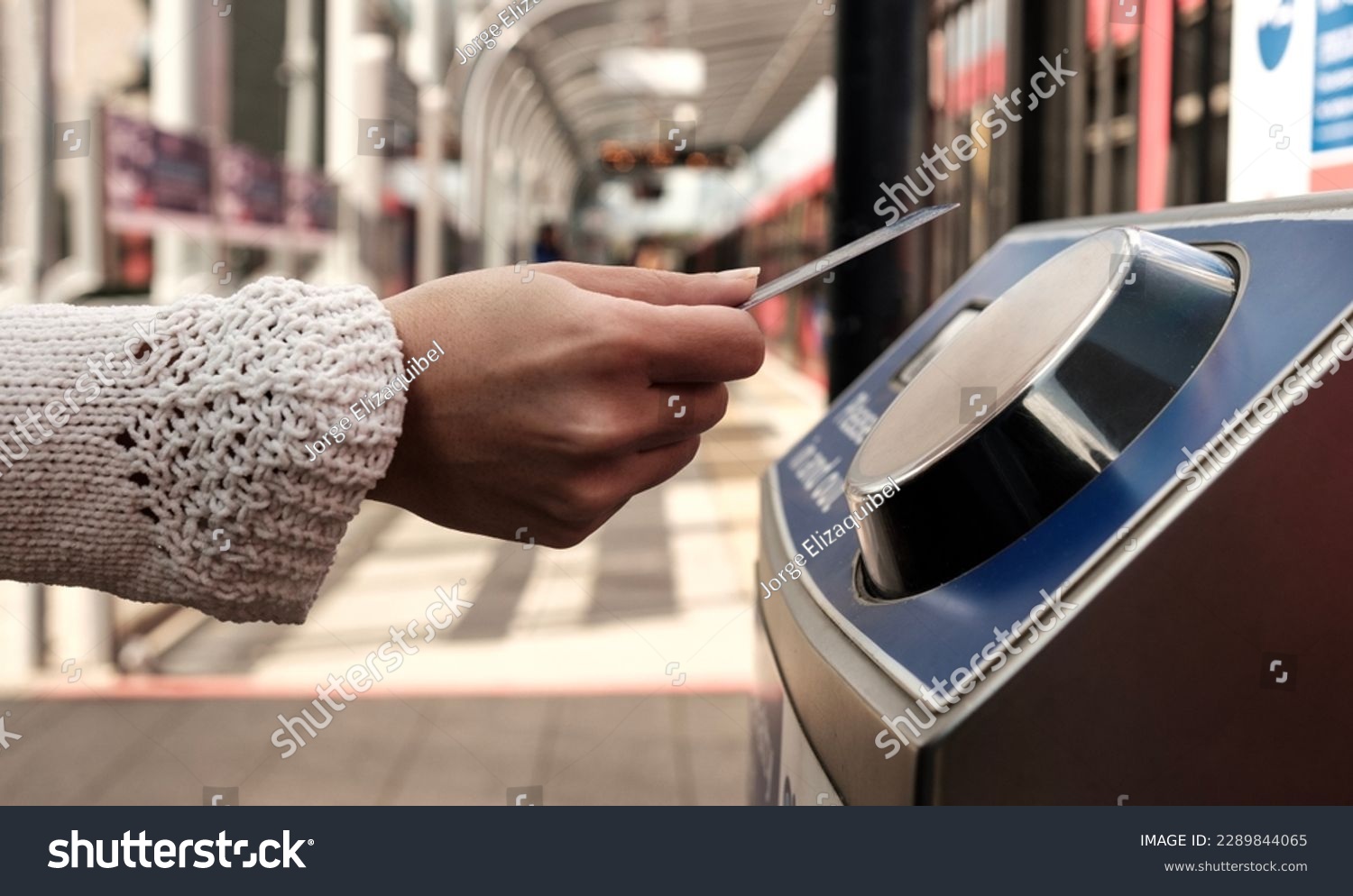 Female hand holding a card on contactless card reader machine in train station in London. There a blurry red train in the station. No cash public transport concept. #2289844065