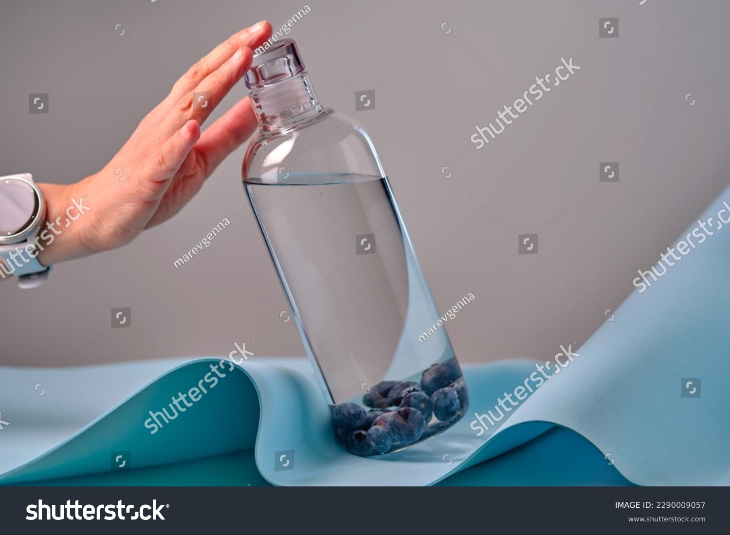 A woman's hand reaches for a glass bottle of water with blueberries. #2290009057