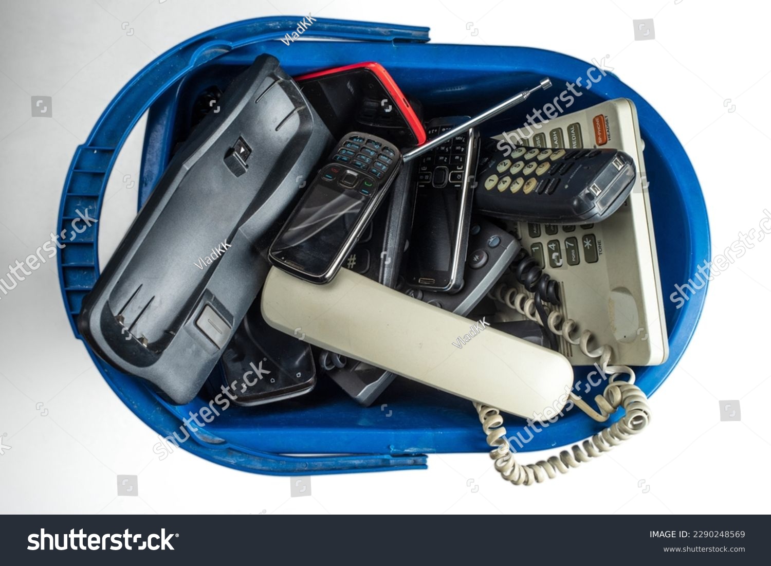 Old desk phones, cordless phone, cell phones, and smartphones in a trash can isolated on a white background. #2290248569