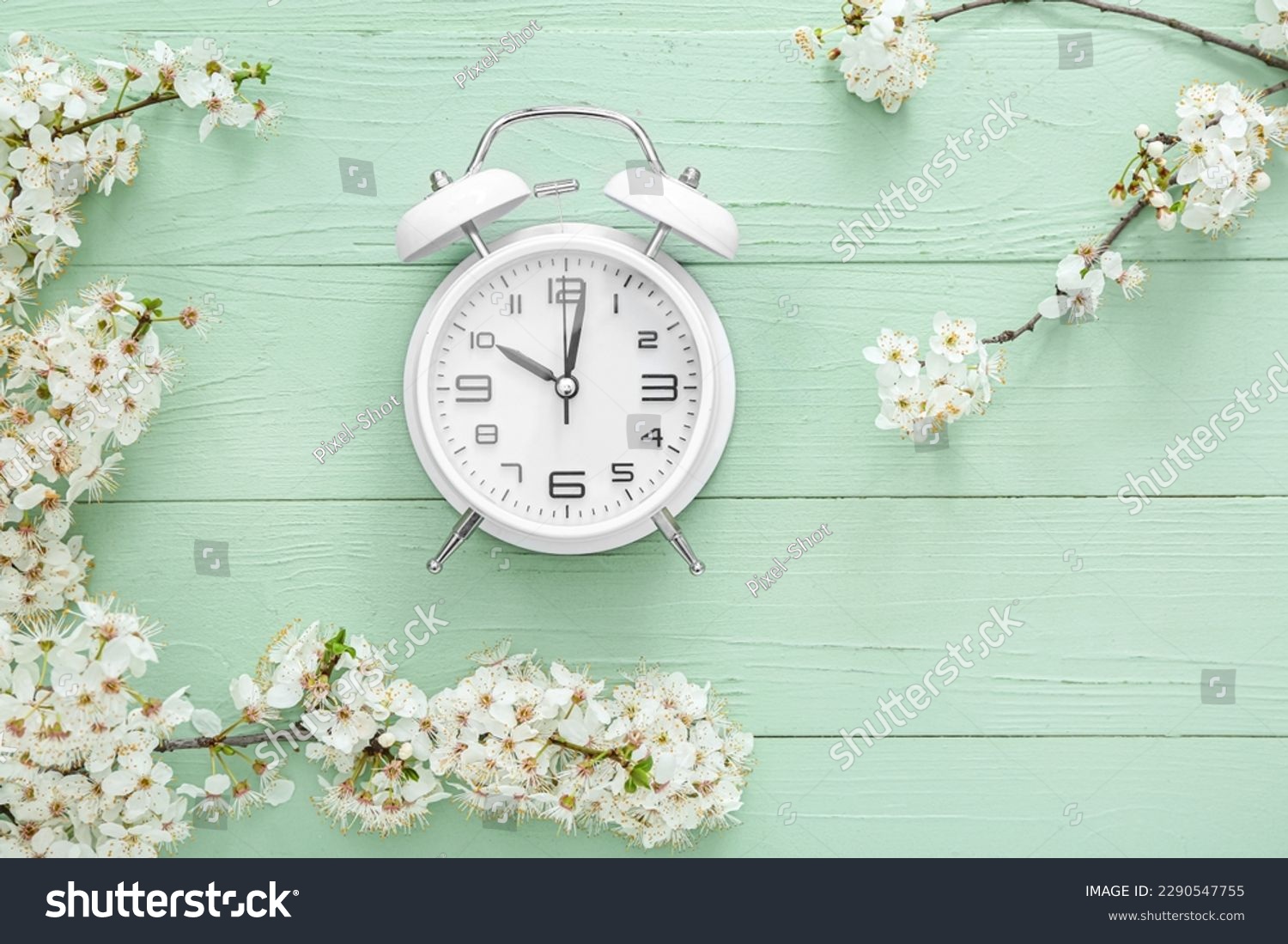 Blooming spring branches and alarm clock on green wooden background #2290547755