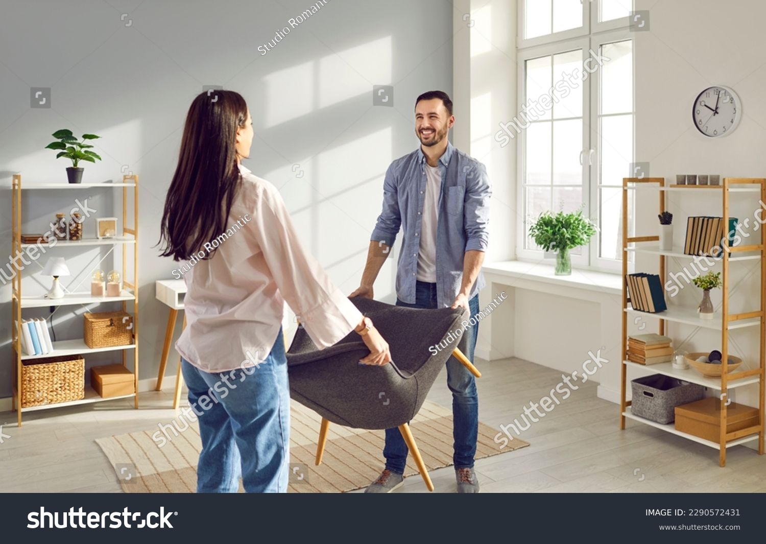 Young couple carrying armchair into their living room. Smiling man and woman moving into new apartment, furnishing and remodeling room. House improvement, remodeling concept #2290572431