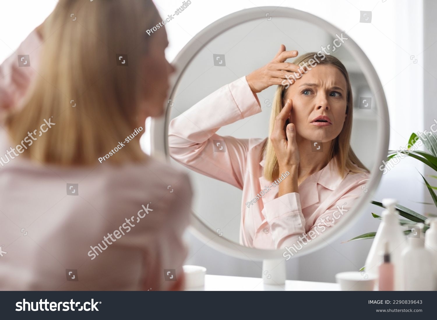 Upset middle aged woman checking wrinkles around her eyes while making beauty routine at home, beautiful mature lady looking in mirror and touching face, feeling tired and stressed, selective focus #2290839643
