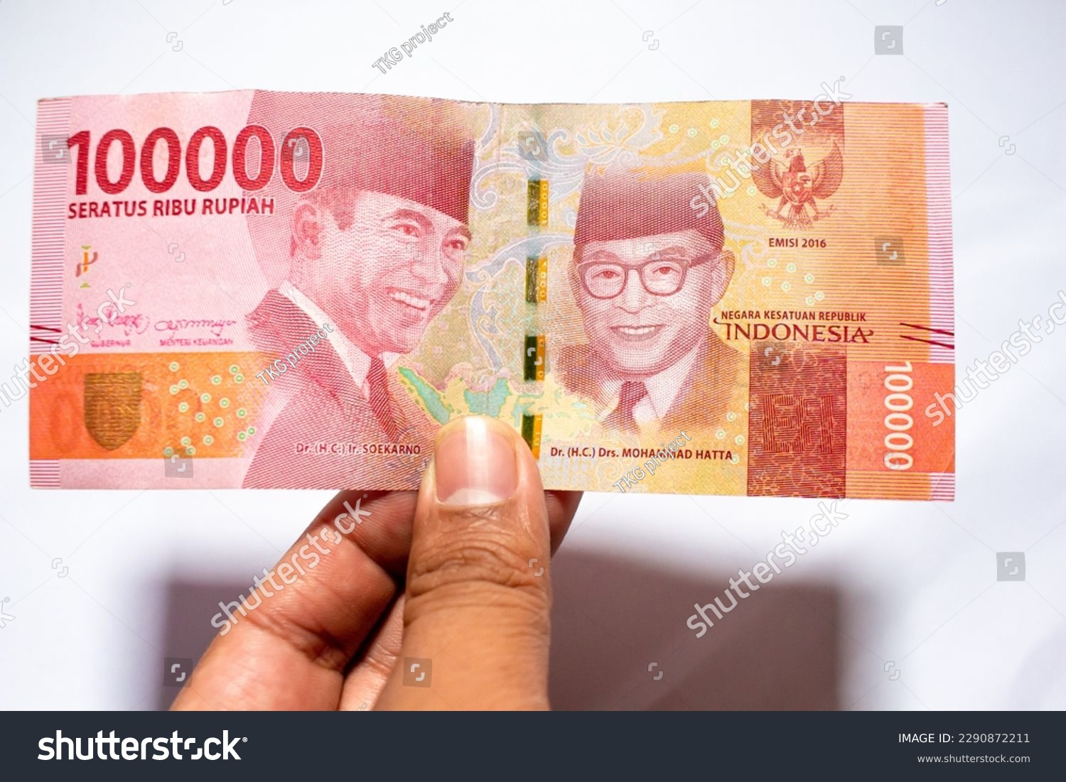 a man's hand is making a payment. Male hand showing Indonesian rupiah note. Indonesian Rupiah the official currency of Indonesia. Uang 100000 Rupiah Bank Indonesia. isolated on white background. #2290872211