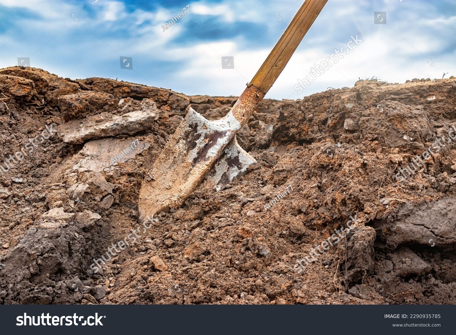 Dirty shovel in fresh soil at a construction site in a pit. Deep hole in the ground. Earthworks, manual refinement of the soil. Dig deep ditches and holes #2290935785