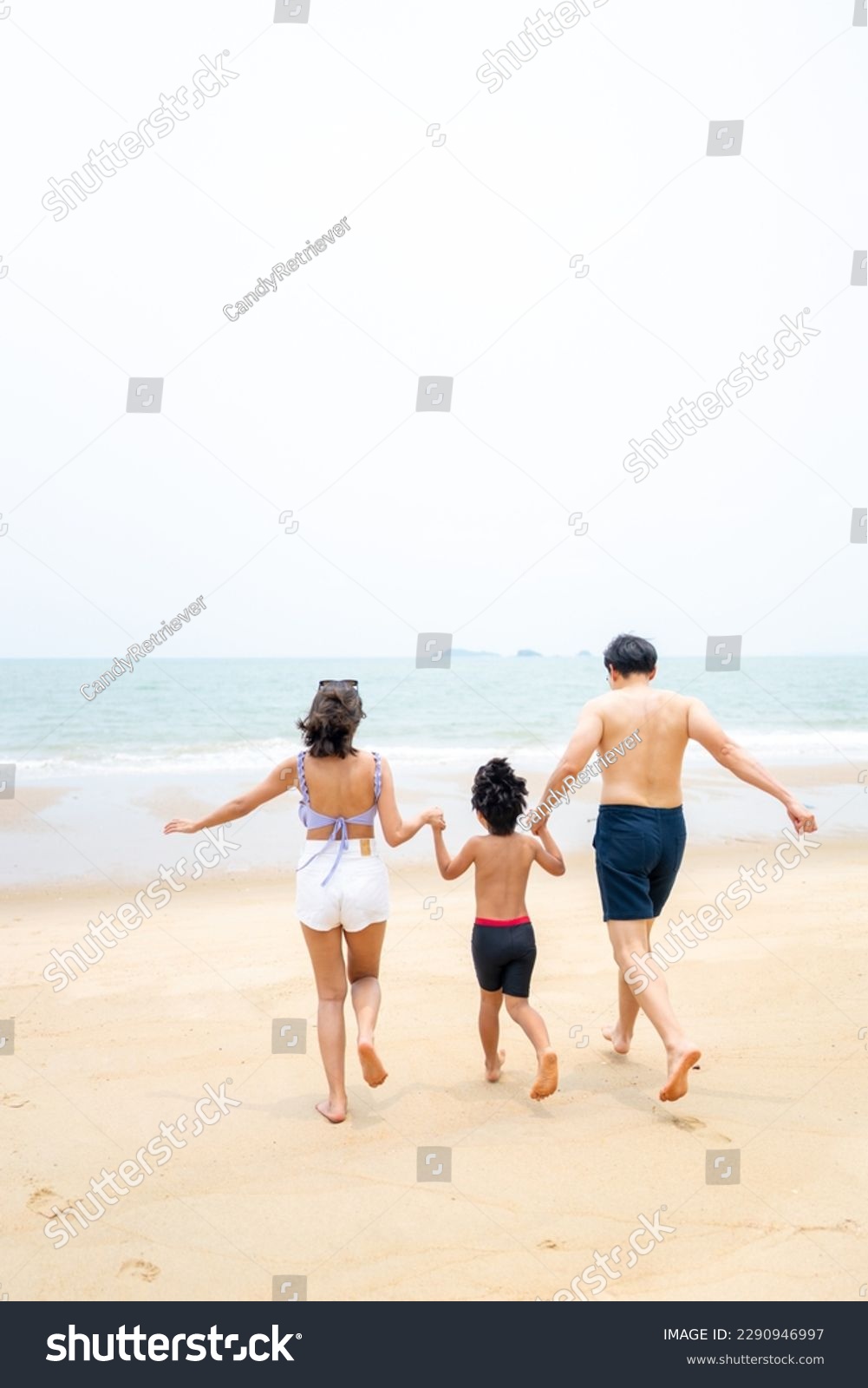 Happy Asian family travel ocean on summer holiday vacation. Parents and little son in swimwear have fun outdoor activity lifestyle walking and playing sea water together at tropical beach in sunny day #2290946997