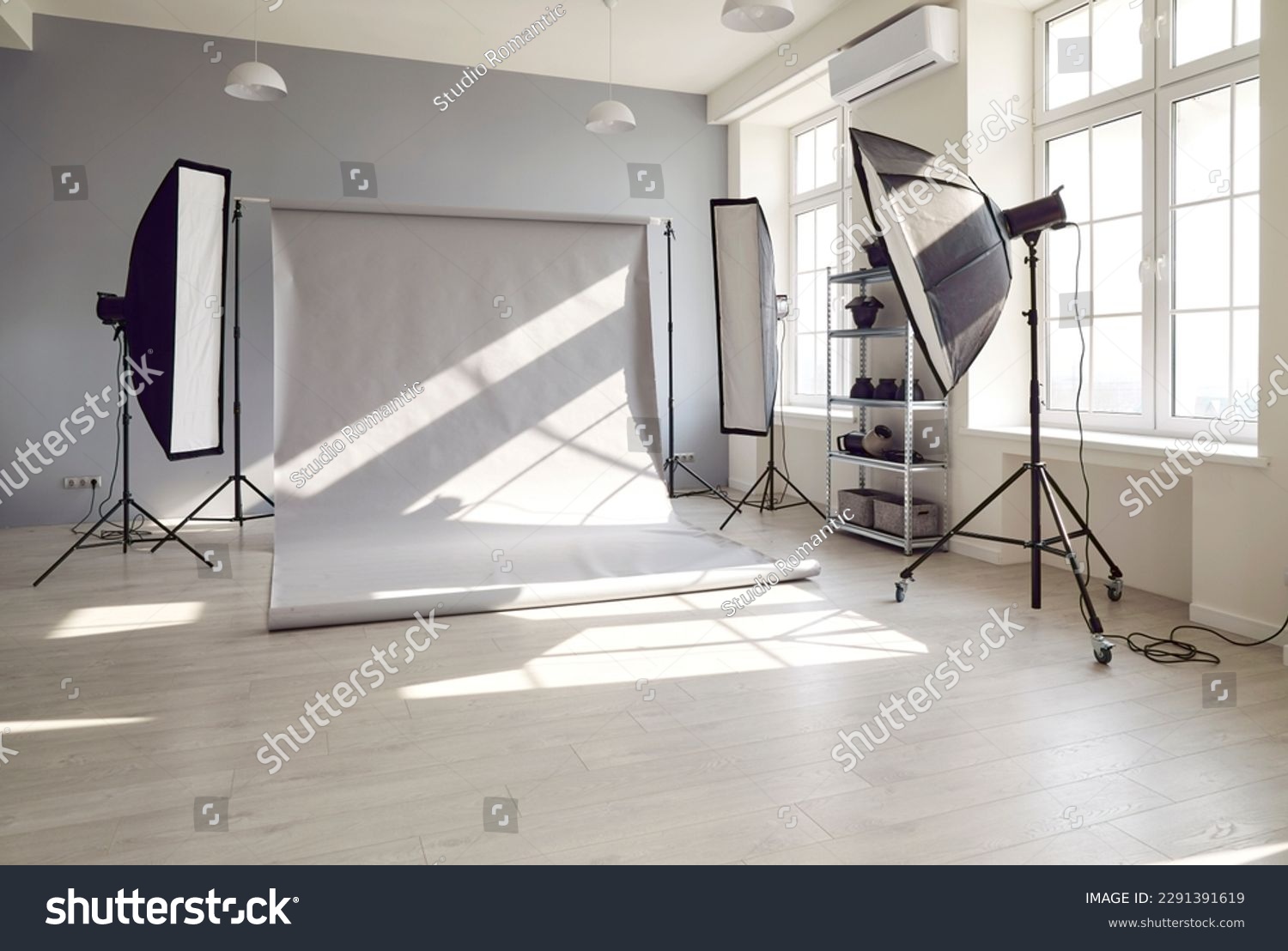 Photo session studio. Photographer's workplace in commercial atelier agency. Sunny workspace interior with grey backdrop, backstage and lamp, umbrella, flashlight illumination equipment kit. No people #2291391619