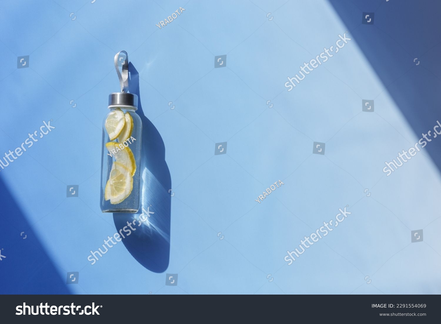 Lemon water drink detox in bottle, hard shadow at sunlight on blue background. Wellness, diet, eating healthy concept. Top view glass reusable water bottle, eco friendly lifestyle, minimal style photo #2291554069