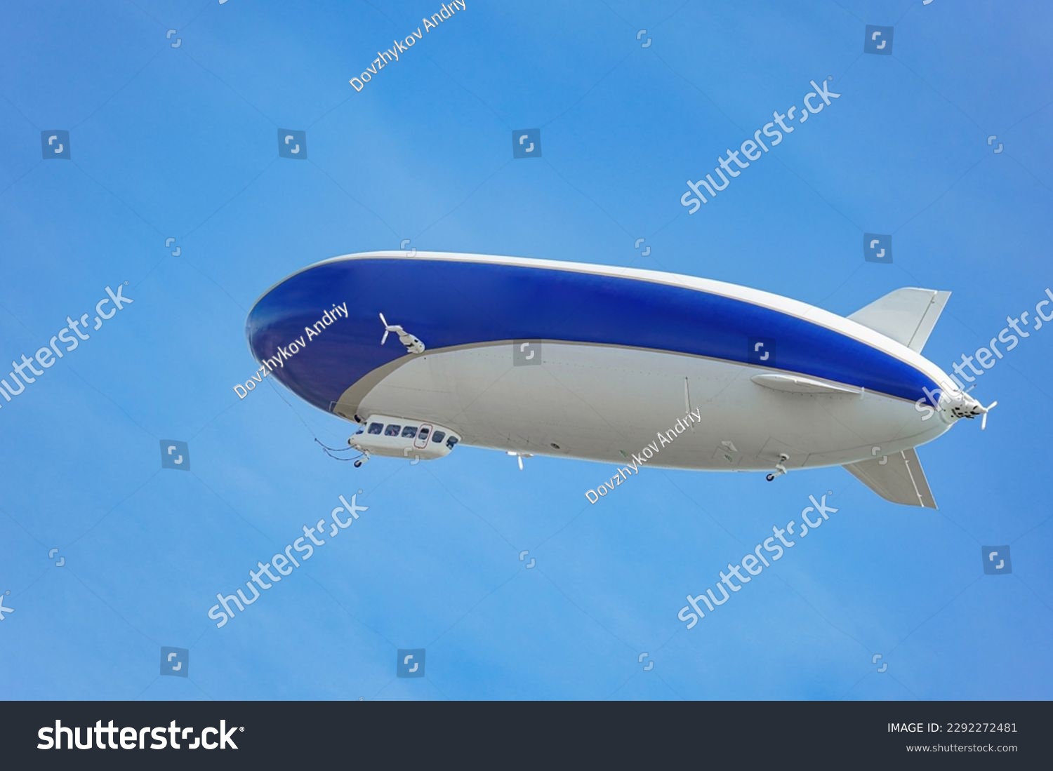 A blue and white airship with passengers on board flies against the blue sky.  #2292272481