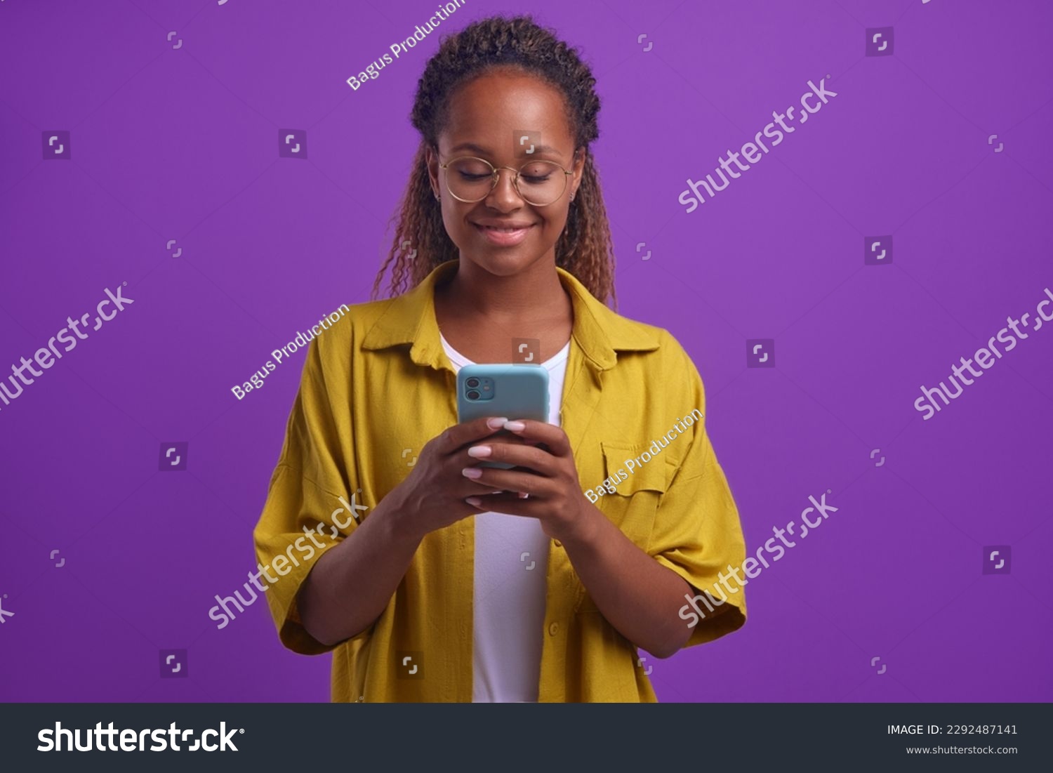 Young positive beautiful African American woman in casual clothes typing text on mobile phone using dating apps or instant messengers to find boyfriend stands on isolated lilac background #2292487141