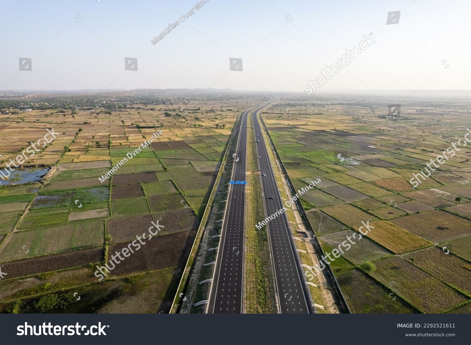 orbit aerial drone shot of new delhi mumbai jaipur express elevated highway showing six lane road with green feilds with rectangular farms on the sides #2292521611