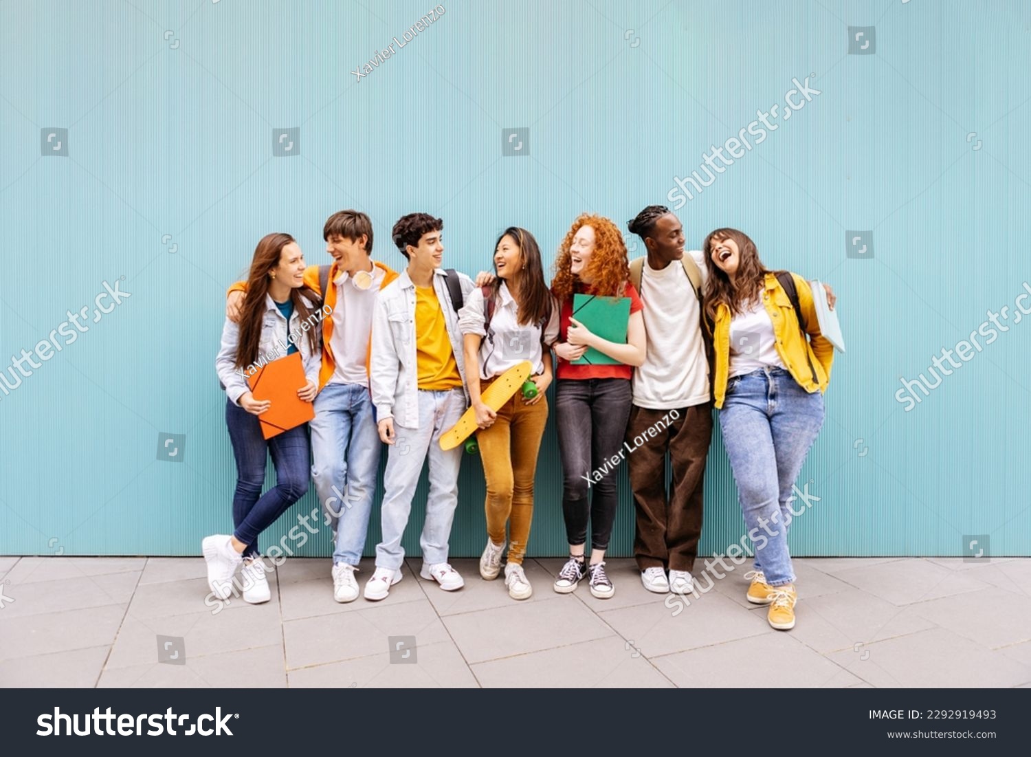 Happy multiracial students standing over isolated blue background. Diverse teenage friends having fun talking leaning on campus building college wall #2292919493