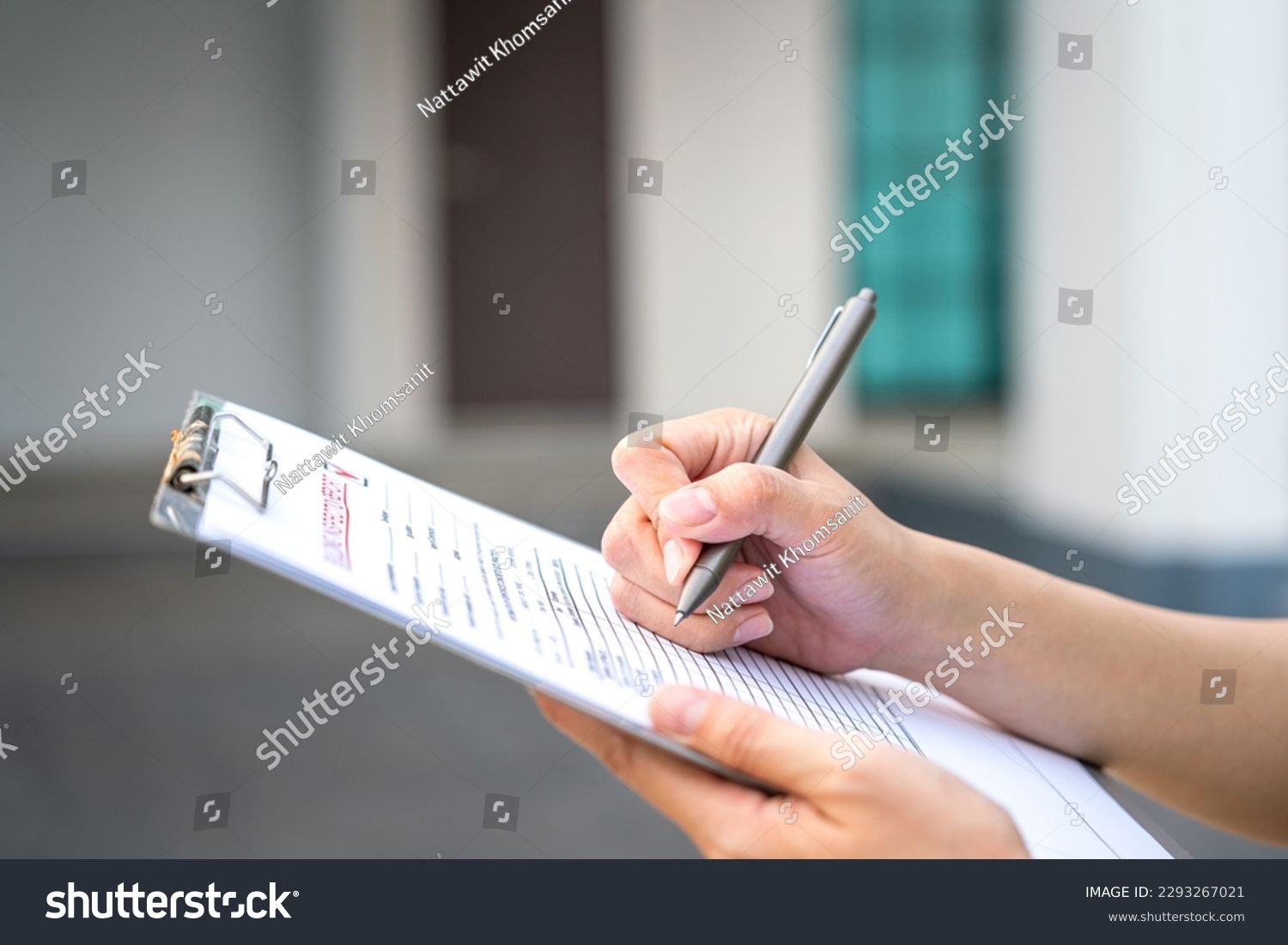 An engineer hand is using a pen checking on the building inspection report form to QC building quality of the house (background). Export industrial working scene concept. Close-up and selective focus. #2293267021