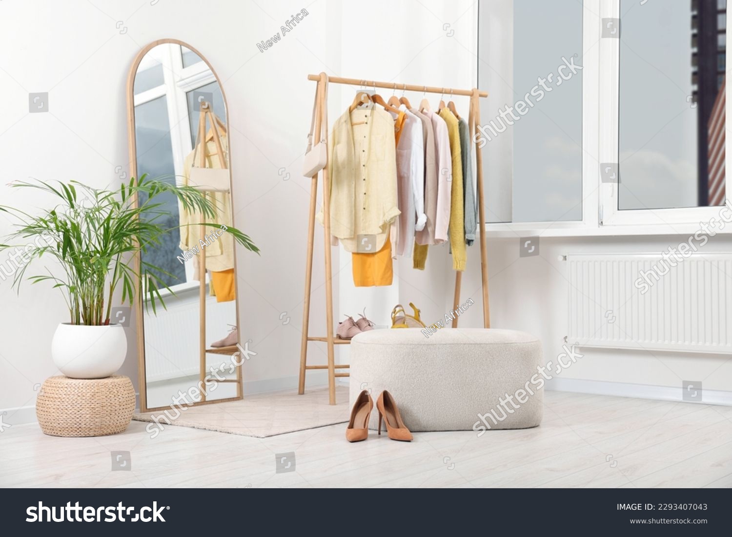 Stylish dressing room interior with mirror, ottoman and clothing rack #2293407043