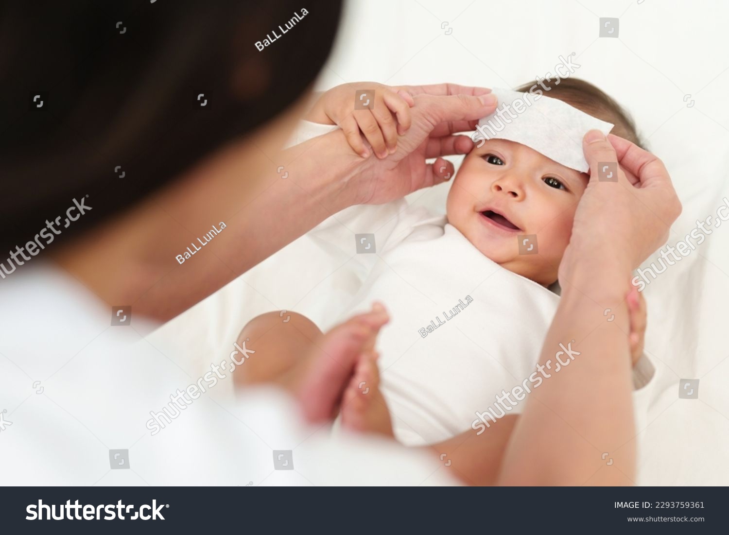 mother putting cool fever jel pad on forehead of happy sick baby  #2293759361