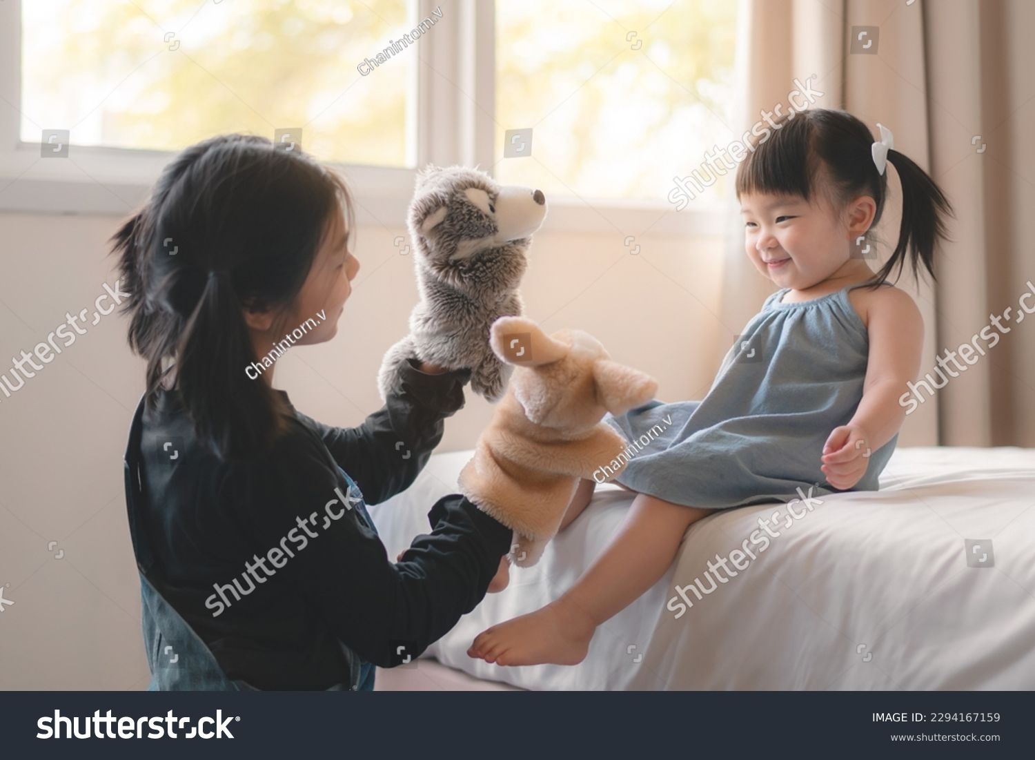 Elder asian sister and younger Asian sister playing animal hand puppet doll toys, sitting on bed, Educational preschool games, Having fun with kid at home concept.; #2294167159